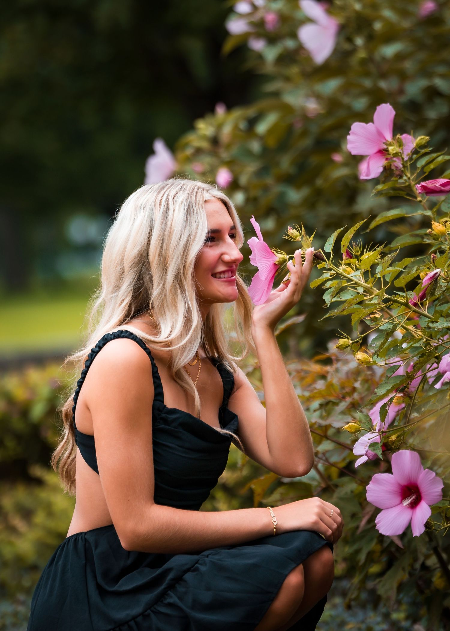 A serene garden portrait of someone in black admiring pink flowers on a sunny day.