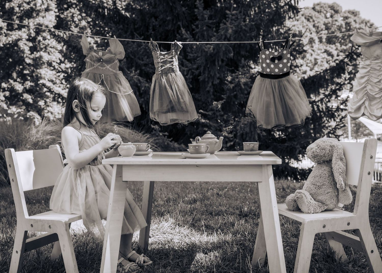 Vintage style photo of tea party setup with dresses hanging on clothesline and stuffed animal guest.