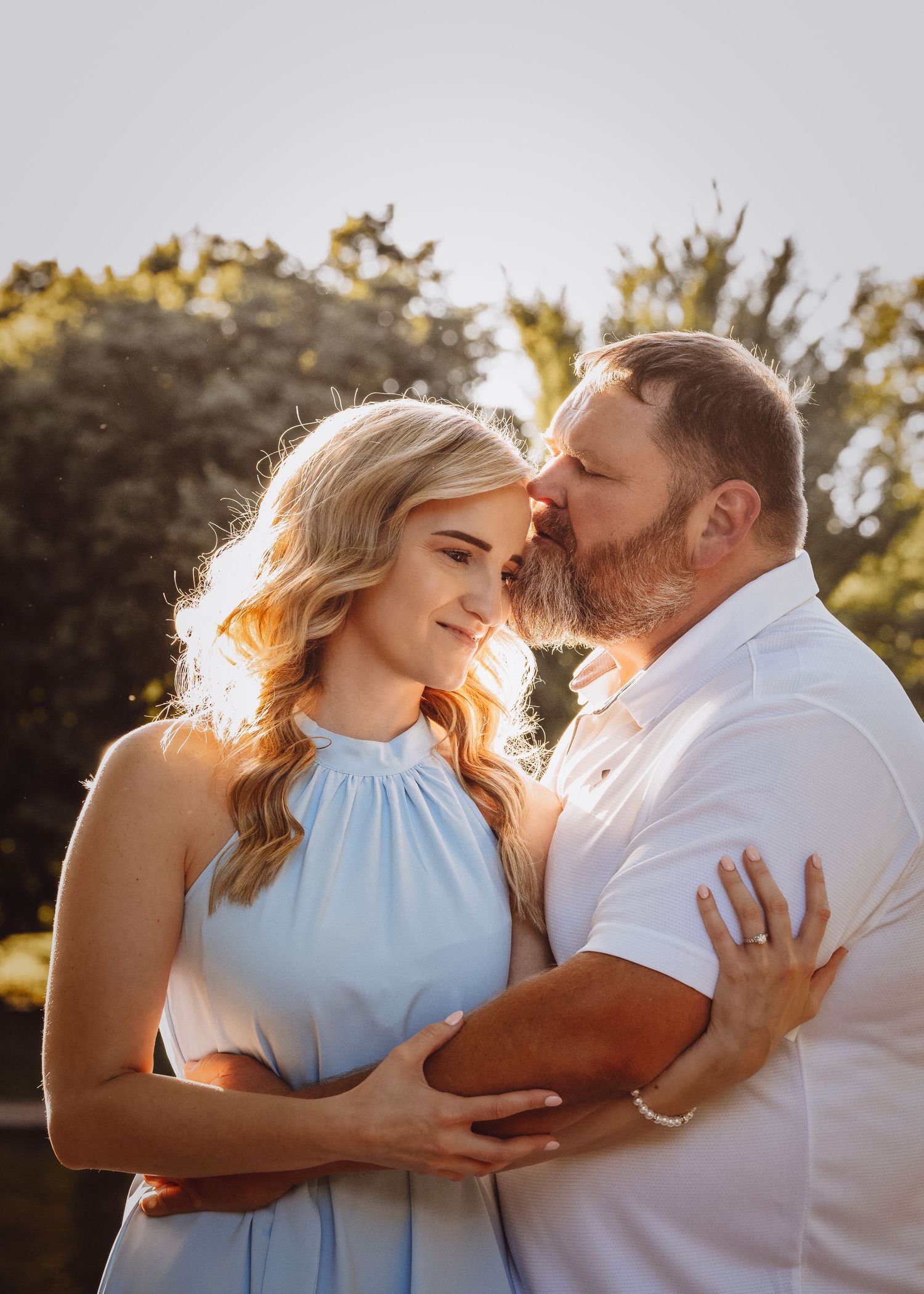 Romantic sunset engagement photo showing tender moment between couple in white and blue outfits.