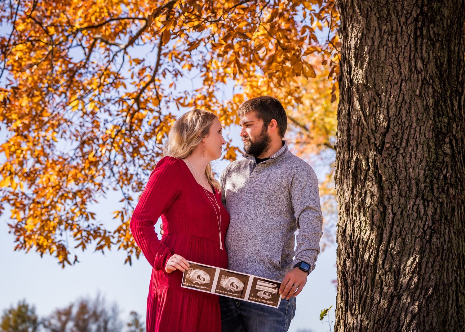 Happy couple embraces under vibrant orange fall foliage during a romantic autumn photoshoot in the forest.