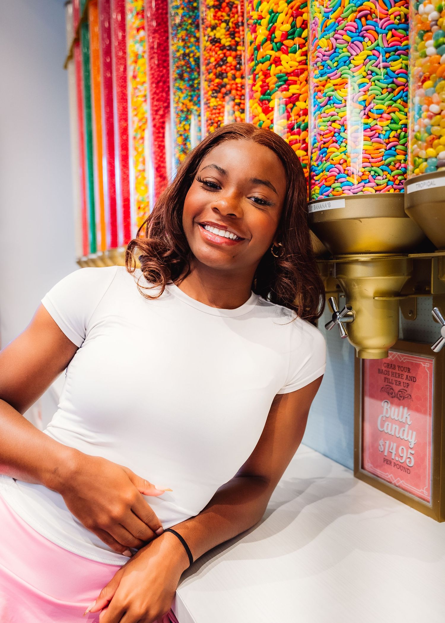A joyful portrait in front of colorful candy dispensers in a sweet shop.