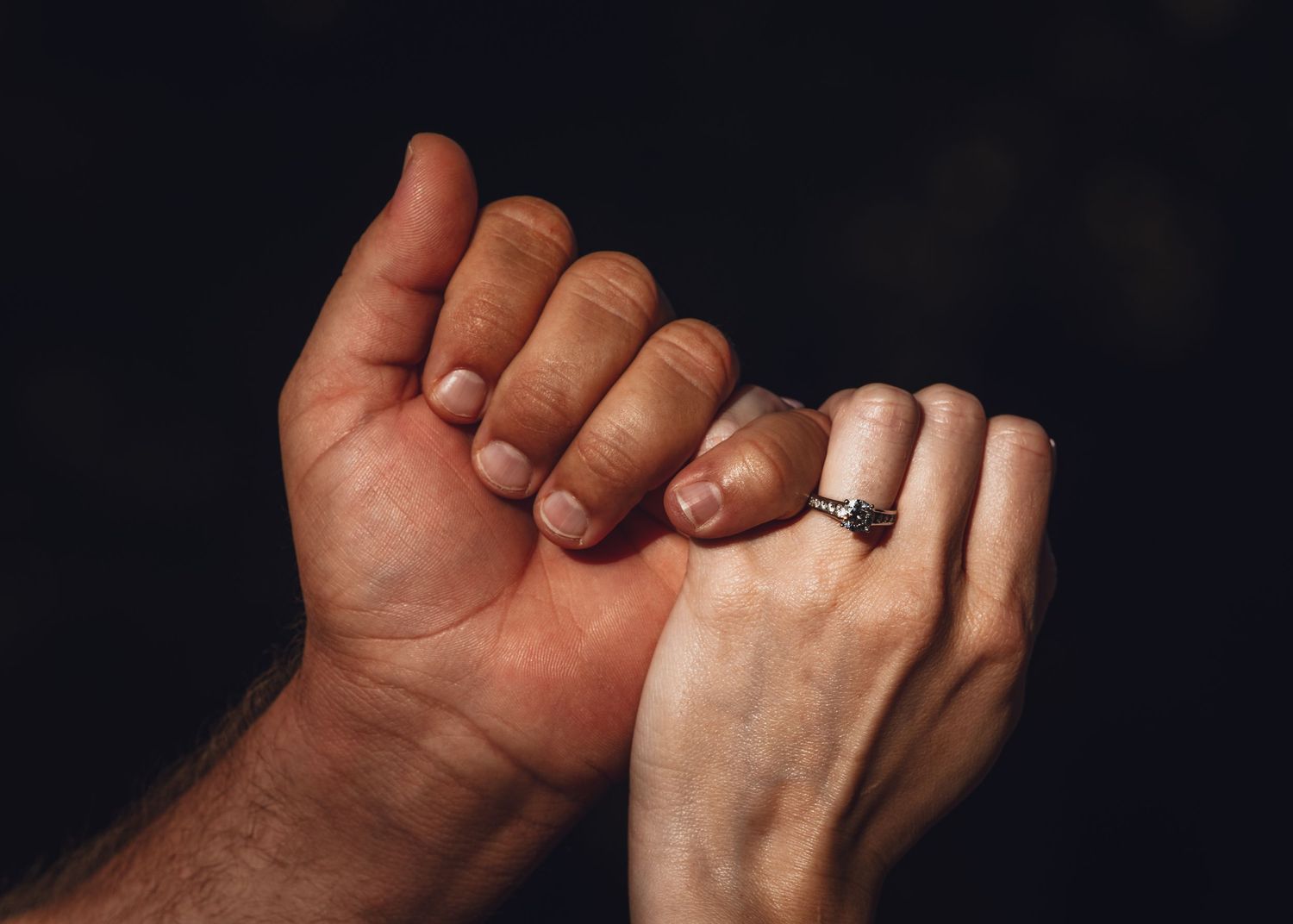 Close-up of intertwined hands with an engagement ring in dramatic lighting.