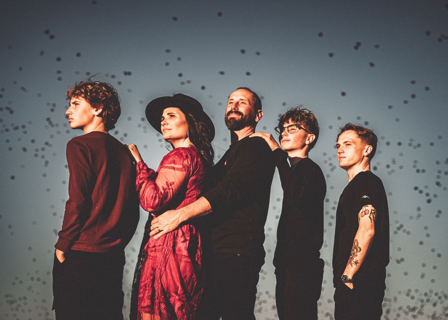 Band members pose dramatically against a twilight sky filled with floating particles.