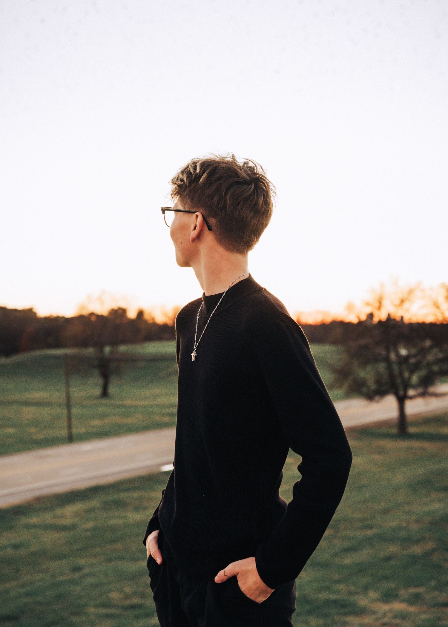 Side profile of someone in black sweater and glasses against sunset backdrop.
