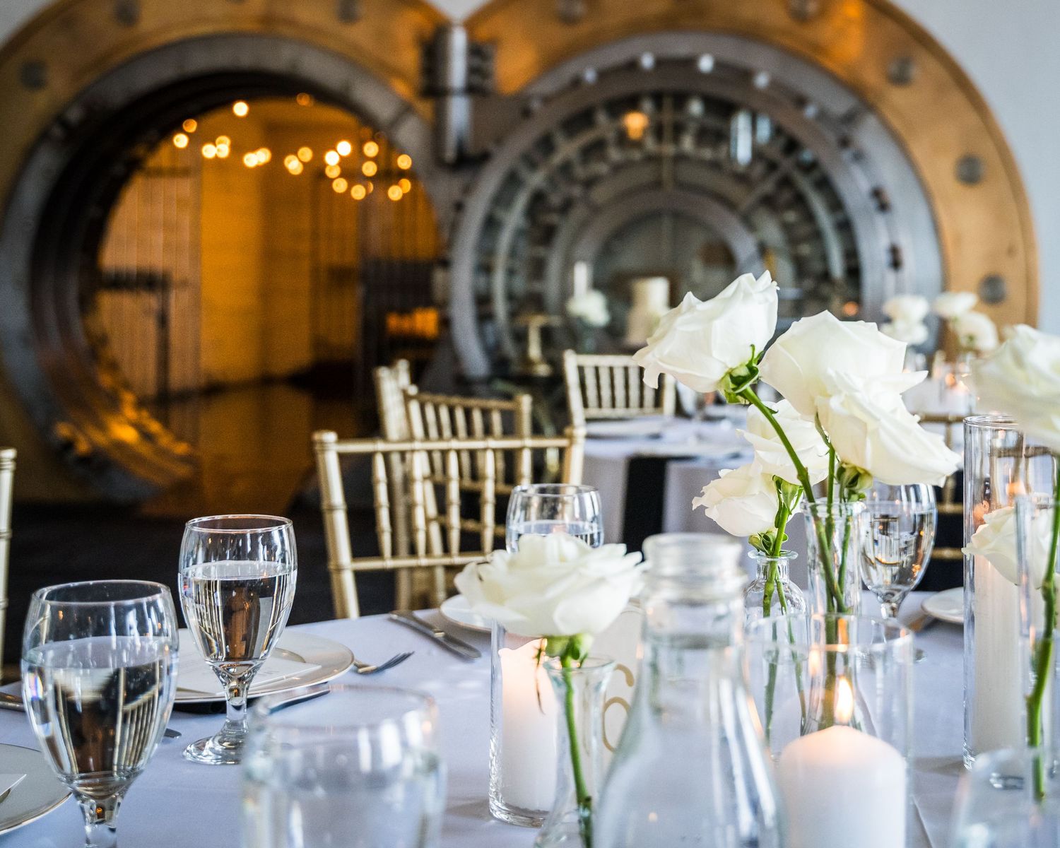 Wedding reception table set with white flowers and glassware in grand venue with arched doorway.