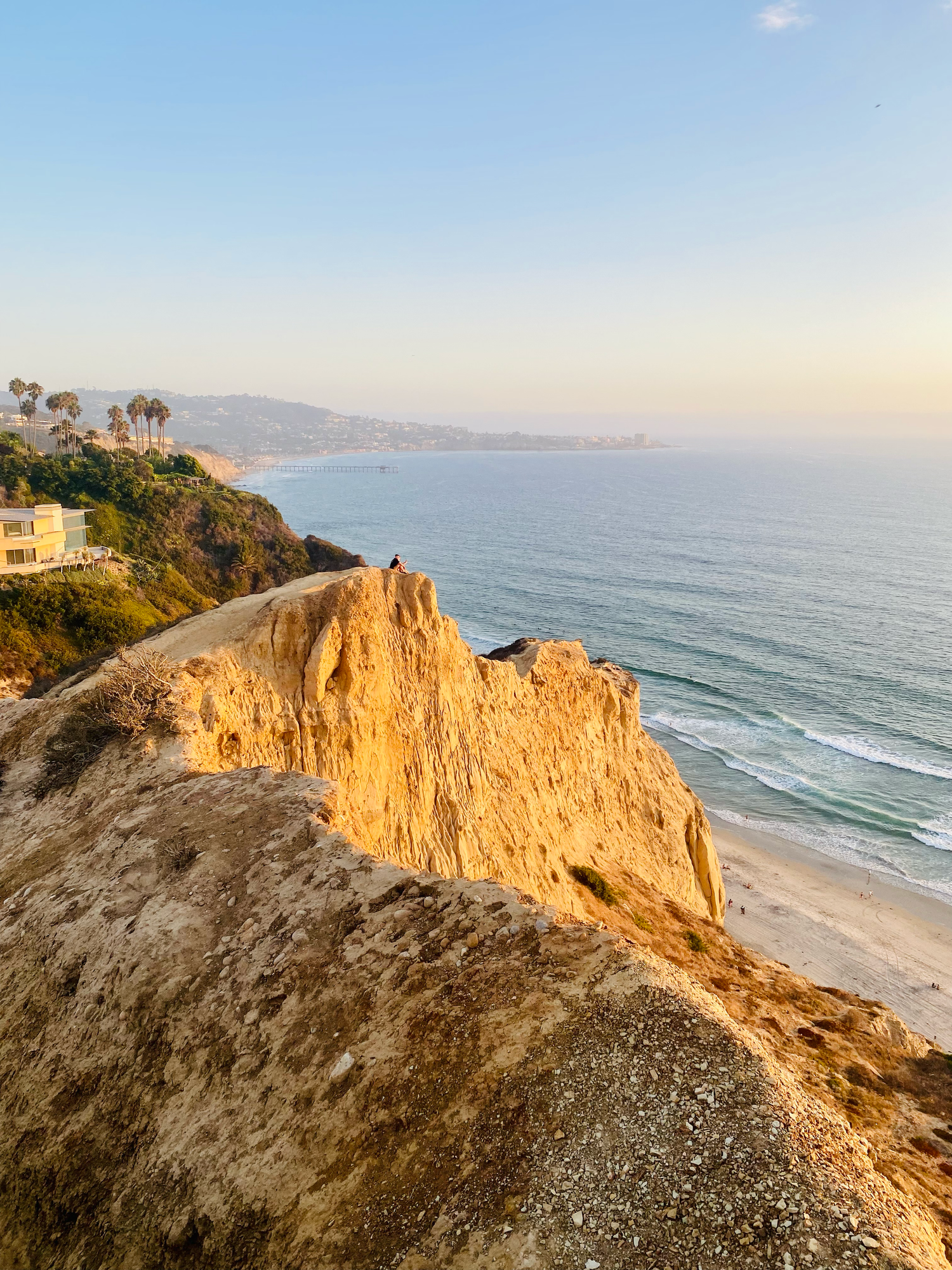 Golden cliffs overlook a sandy beach and turquoise ocean at sunset along the Southern California coastline.