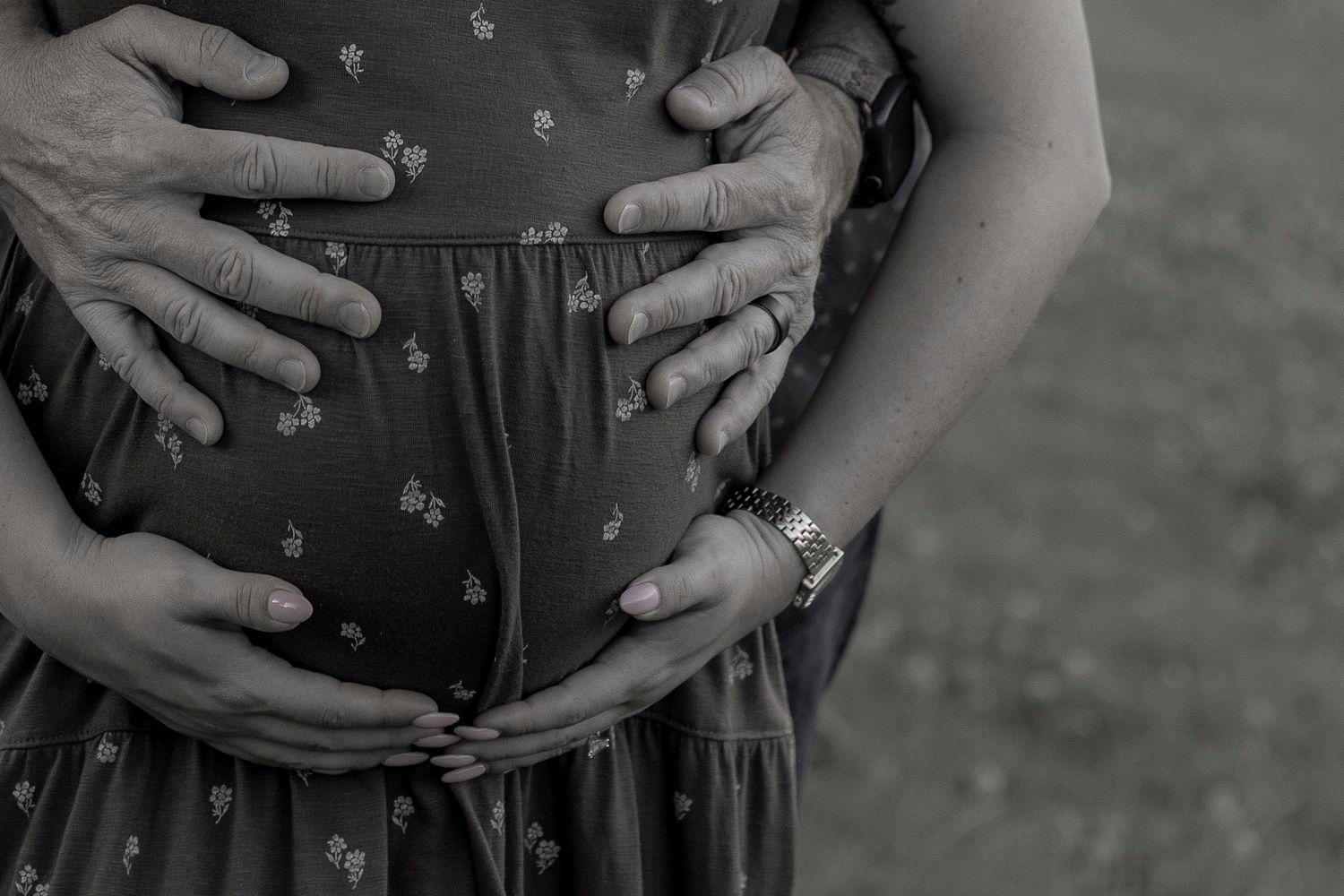Black and white close-up of a couple tenderly holding a pregnant belly, showcasing a wedding ring. San Diego photographer