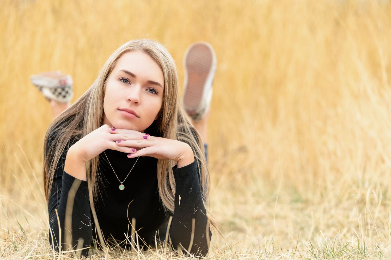Senior girl lying in golden grass field in North Salt Lake with soft light and relaxed pose in natural outdoor setting
