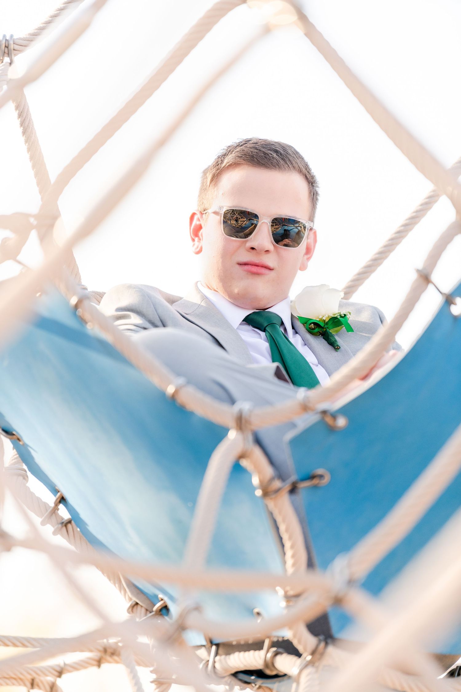 Senior boy portrait through playground bars wearing sunglasses and blue suit