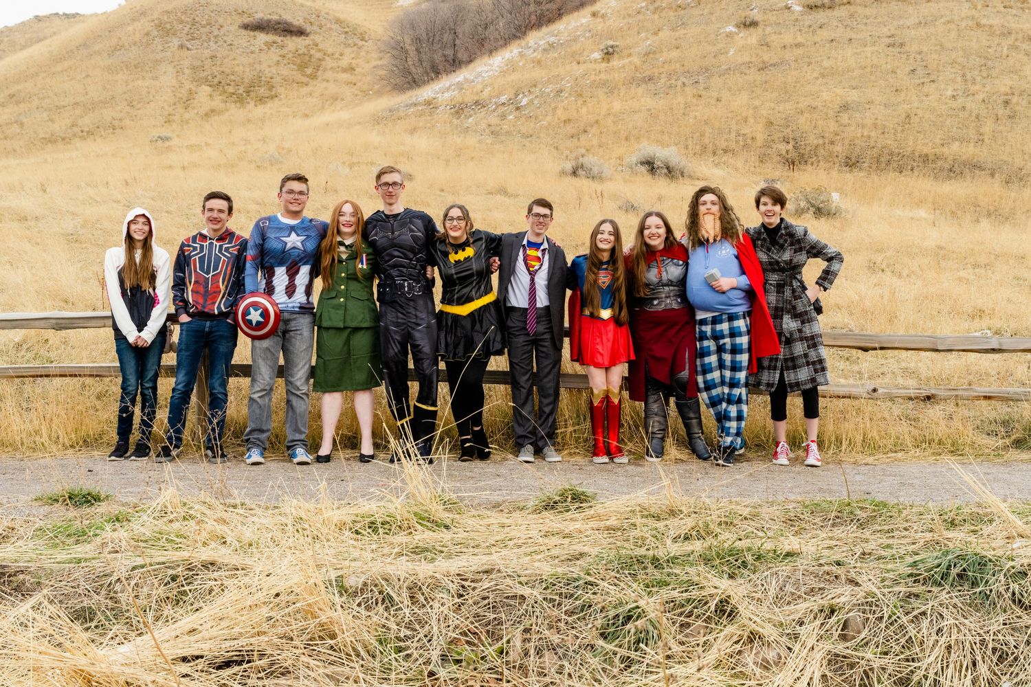 Large group of teens posing outdoors in super hero themed outfits with hillside background for Sadie Hawkins Woods Cross dance