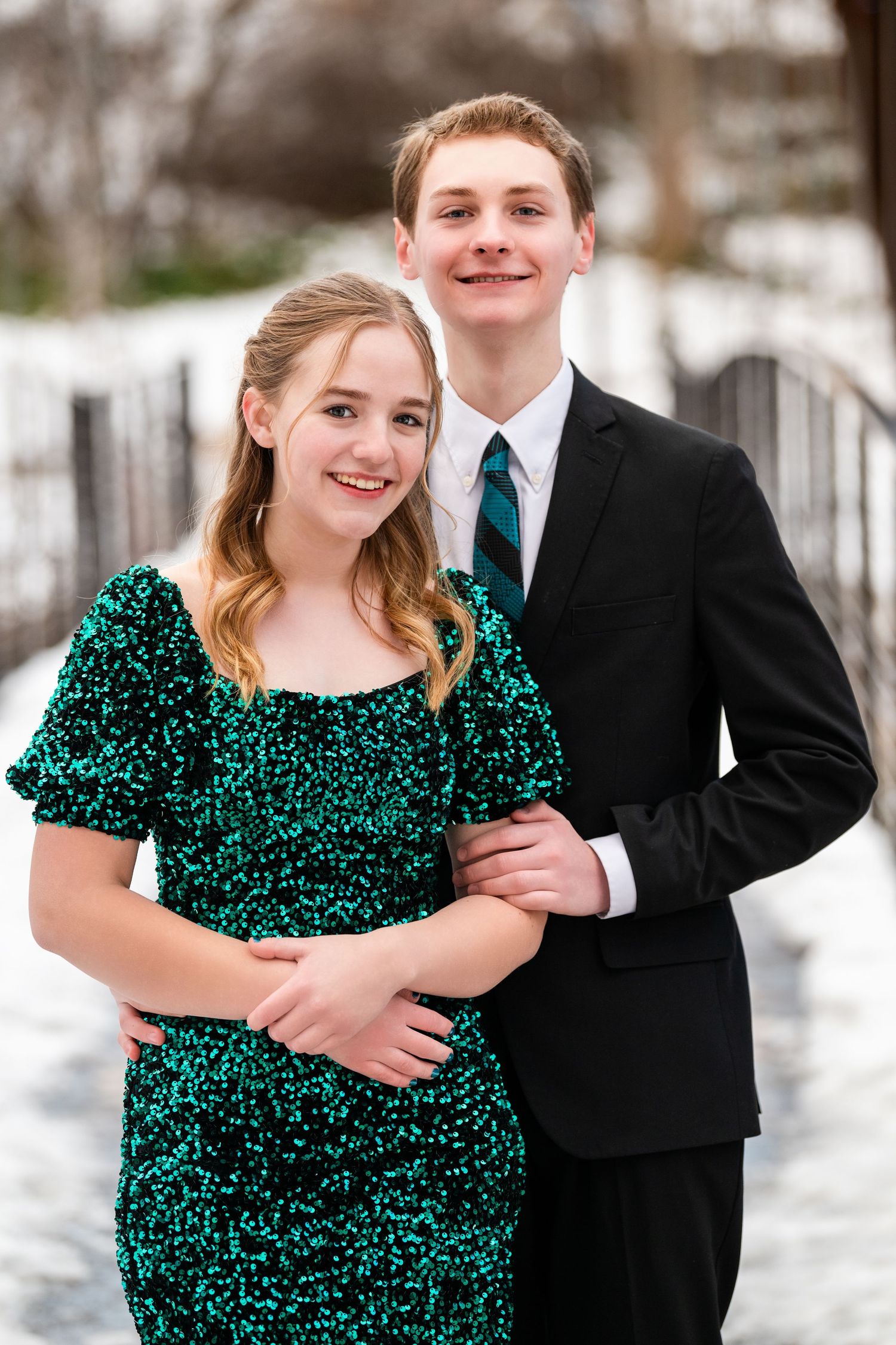 Teen couple posing together in winter setting for Sweethearts dance with green dress and black suit