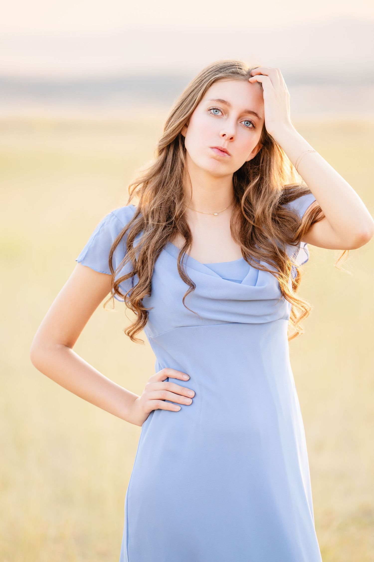 High school girl in blue dress posing in field with soft sunset tones and natural light