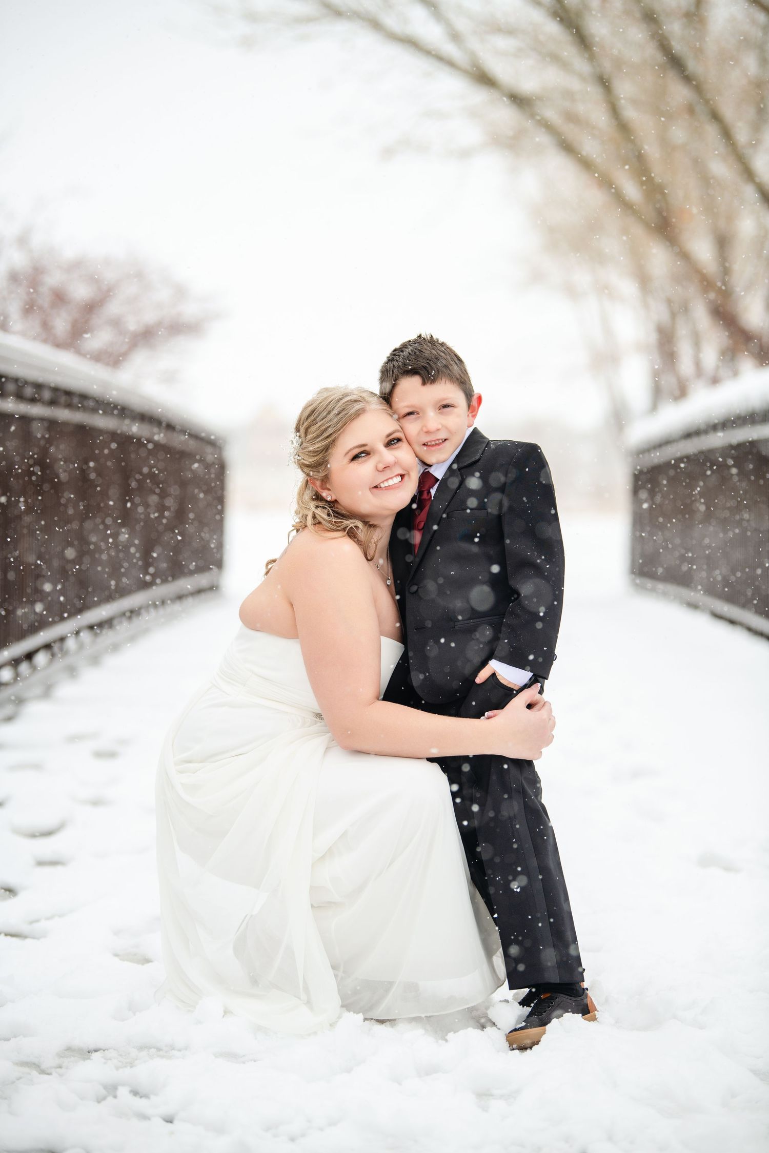 Wedding bride embracing her son on a Salt Lake snowy bridge in Utah with soft snowfall and romantic winter atmosphere