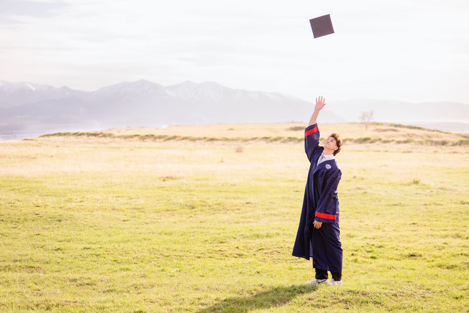 Graduation cap toss photo in open Utah field during Class of 2025 senior graduation session