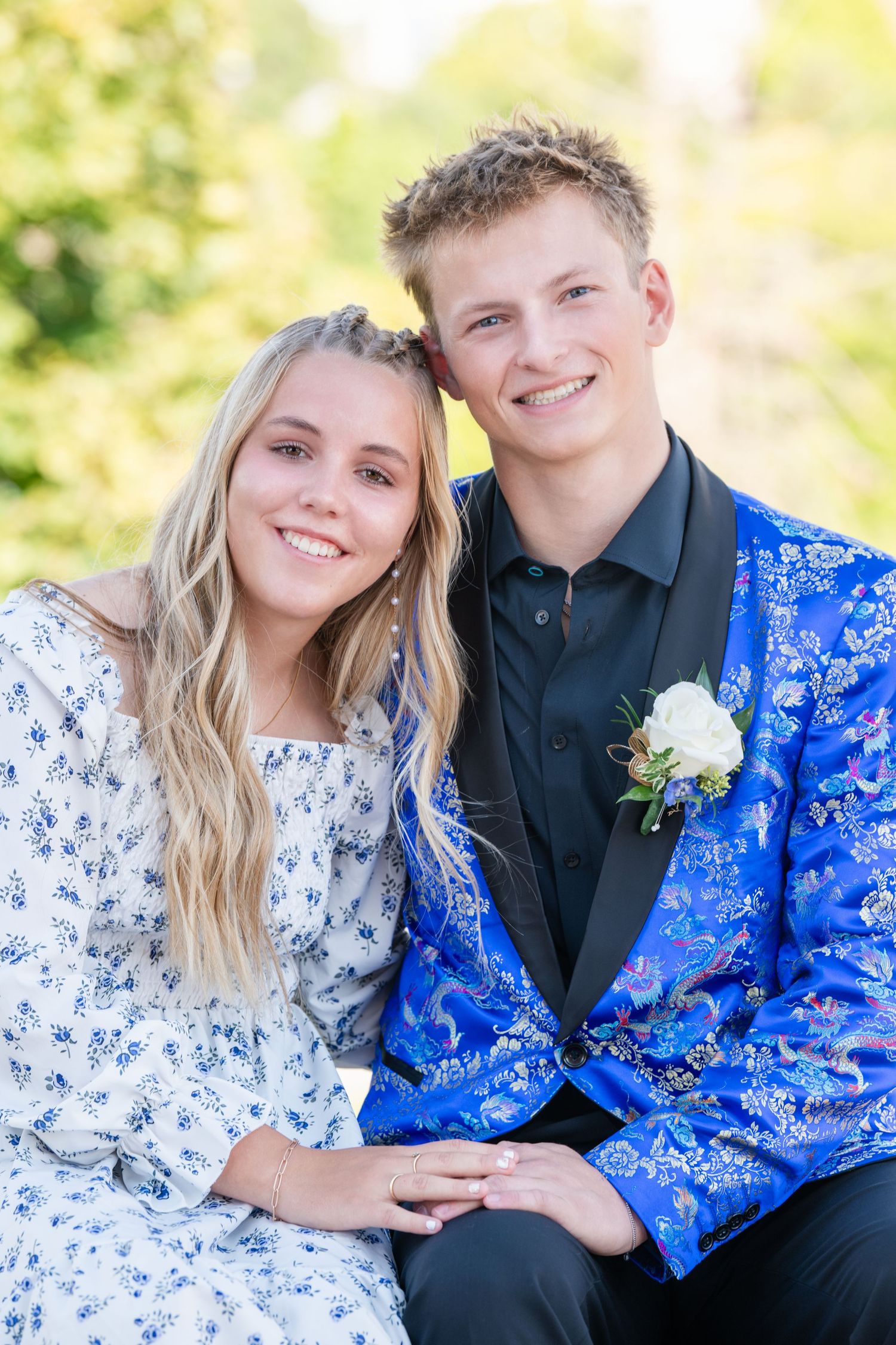 Teen couple sitting close together smiling in formal attire with soft background