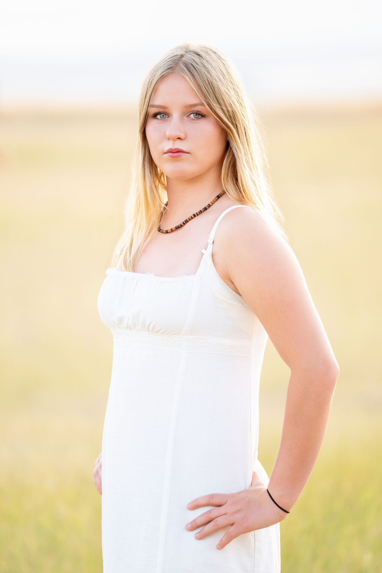 High School girl in white dress standing in open field with soft golden light and neutral tones