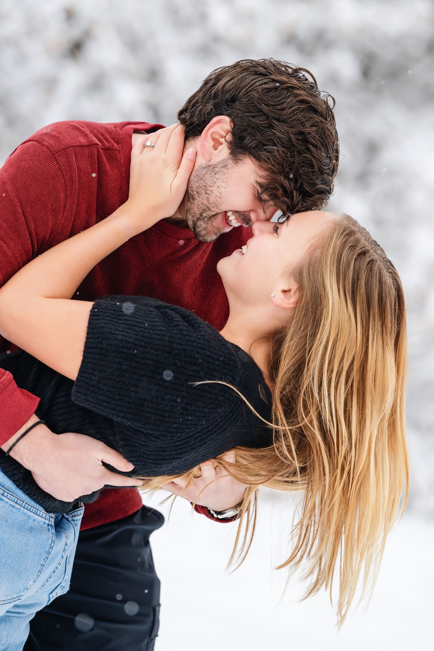 Romantic winter engagement portrait of couple kissing in snowy outdoor setting
