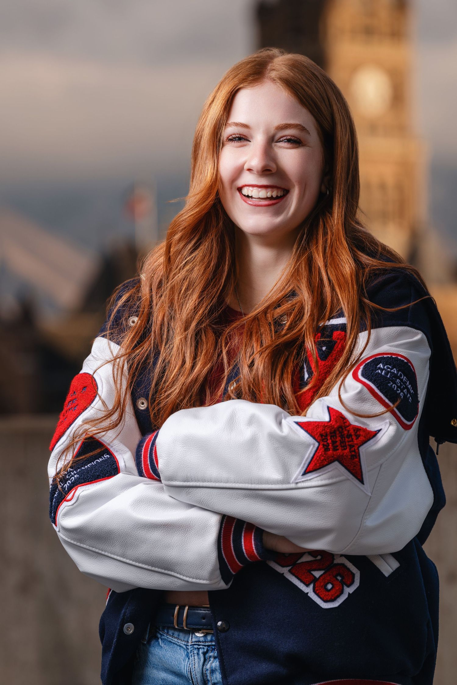 Senior girl smiling in letterman jacket with Salt Lake City background and warm evening light