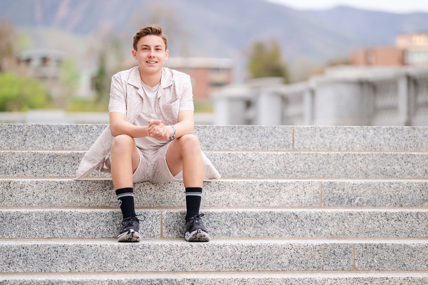 Senior boy sitting on outdoor steps during modern Utah senior portrait session with mountain backdrop