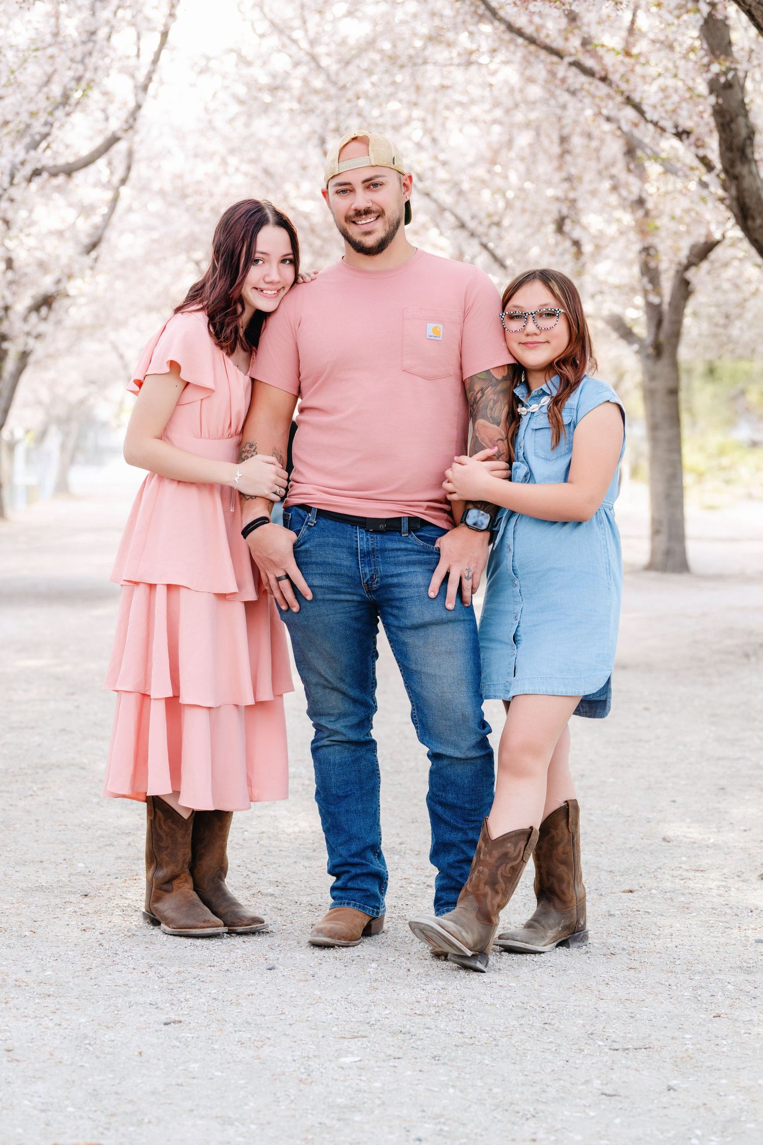 Father with daughters posing beneath blooming spring trees during outdoor family portrait session