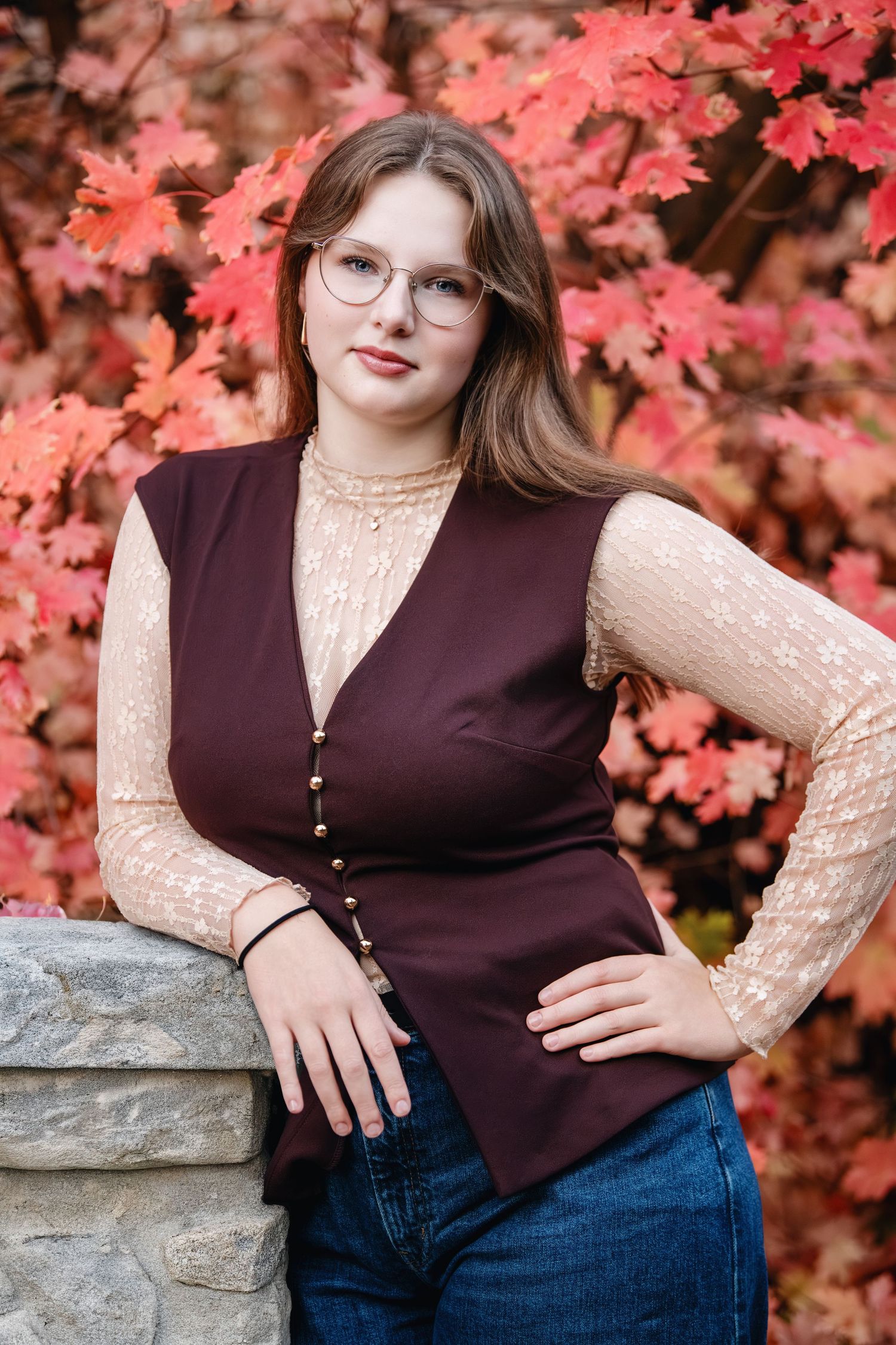 High school senior girl portrait in Bountiful, Utah with red leaves backdrop wearing maroon top and confident pose