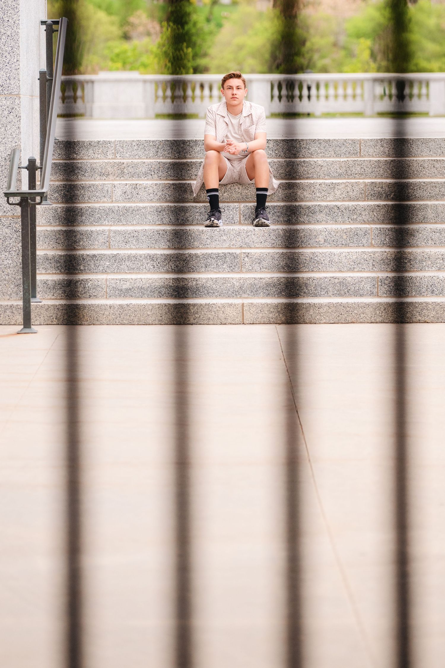 Senior boy sitting on the Salt Lake Capitol steps framed by foreground bars with shallow depth of field