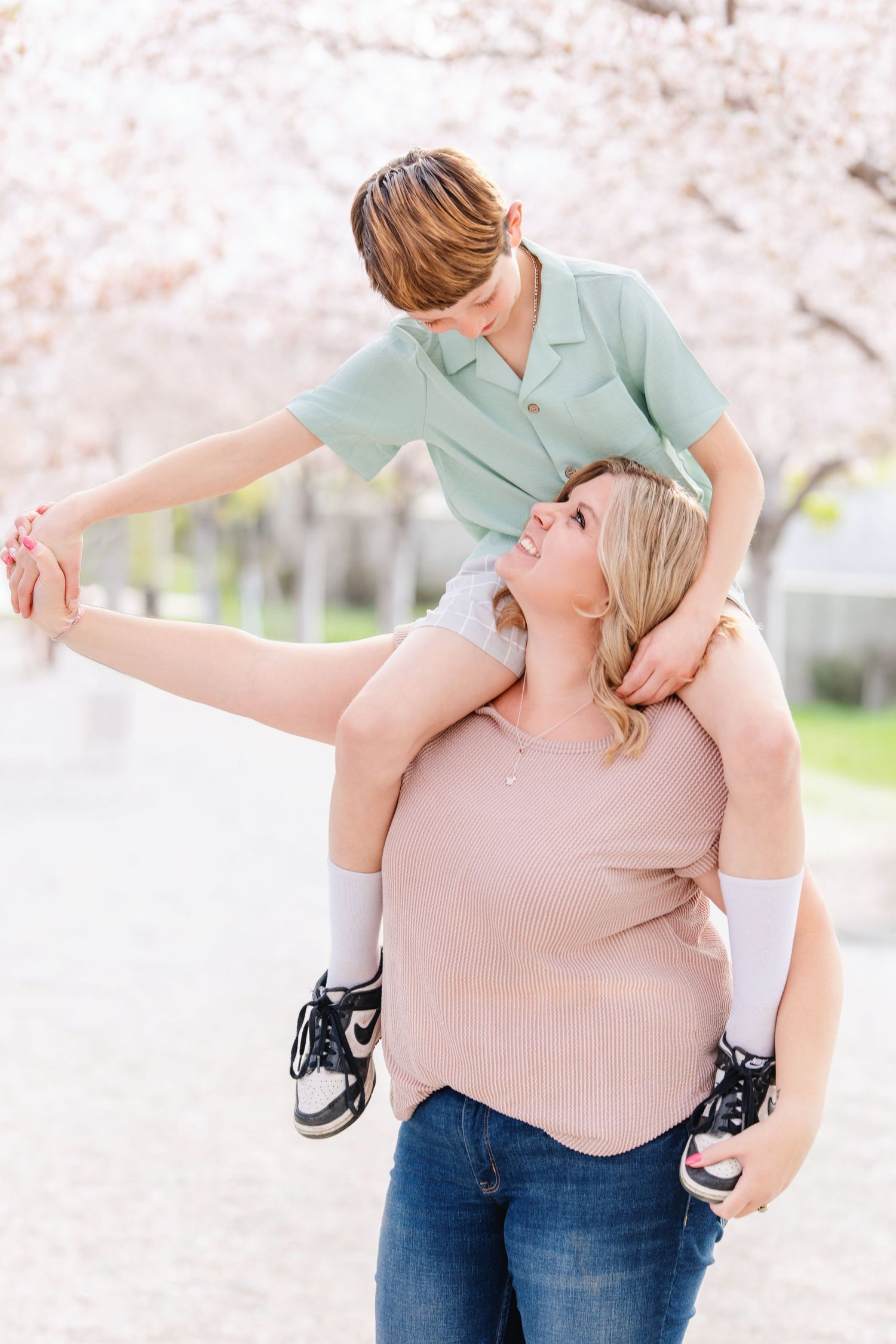 Mother carrying son on shoulders beneath blooming spring trees during family photography session