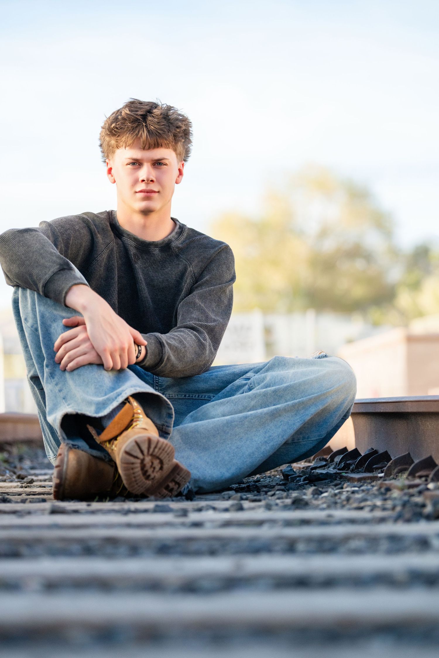 Senior boy sitting on railroad tracks during outdoor Class of 2026 portrait session
