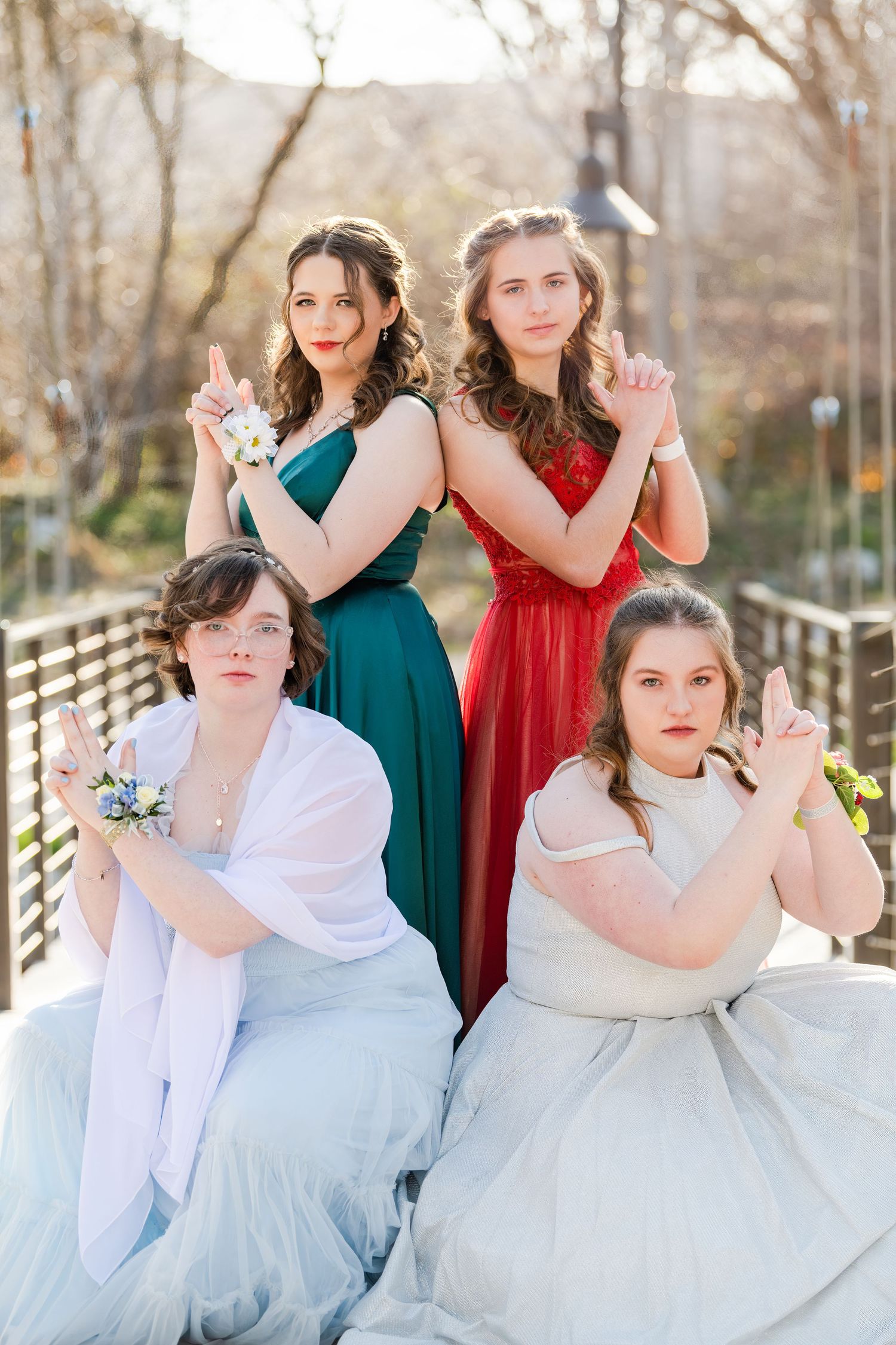 Group of four girls in formal Woods Cross high school prom dresses posing on bridge with soft natural light