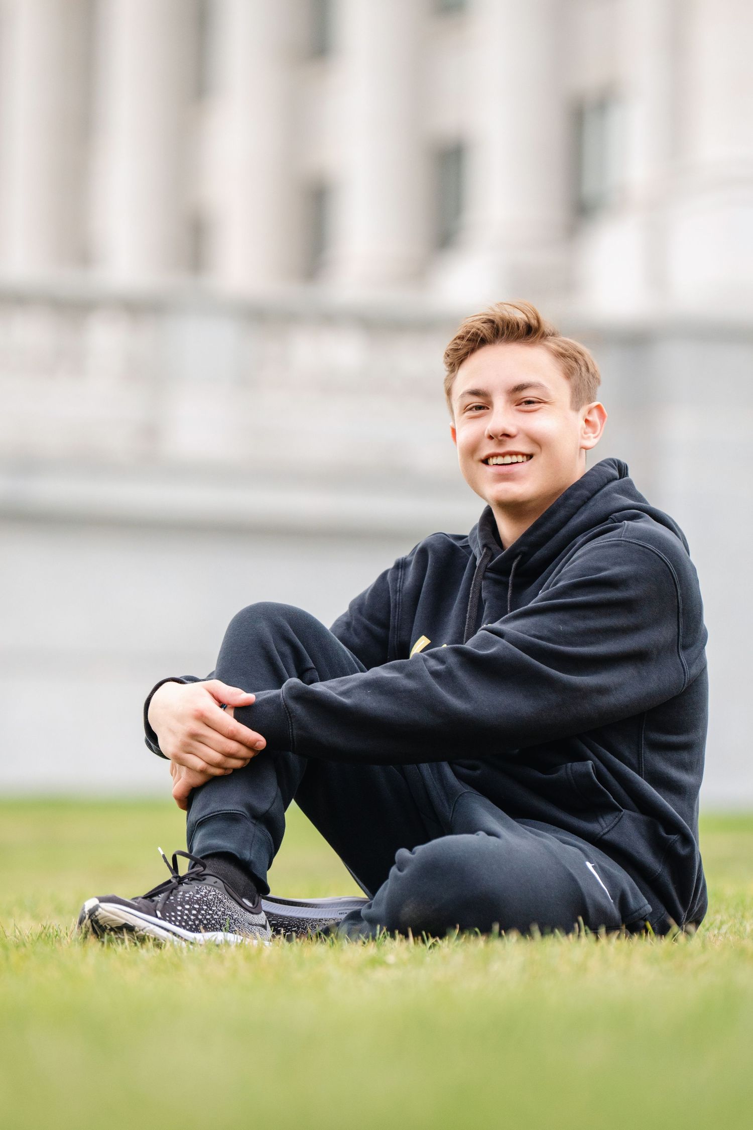 Casual senior portrait of teenage boy sitting on grass during outdoor Class of 2025 photography session