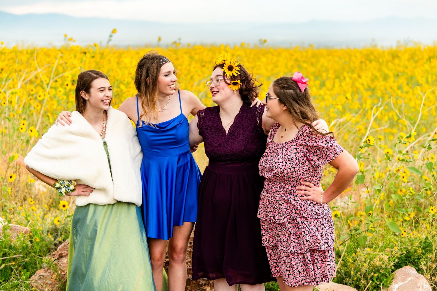 Four girls in colorful dresses standing together in bright yellow flower field during Woods Cross homecoming dance