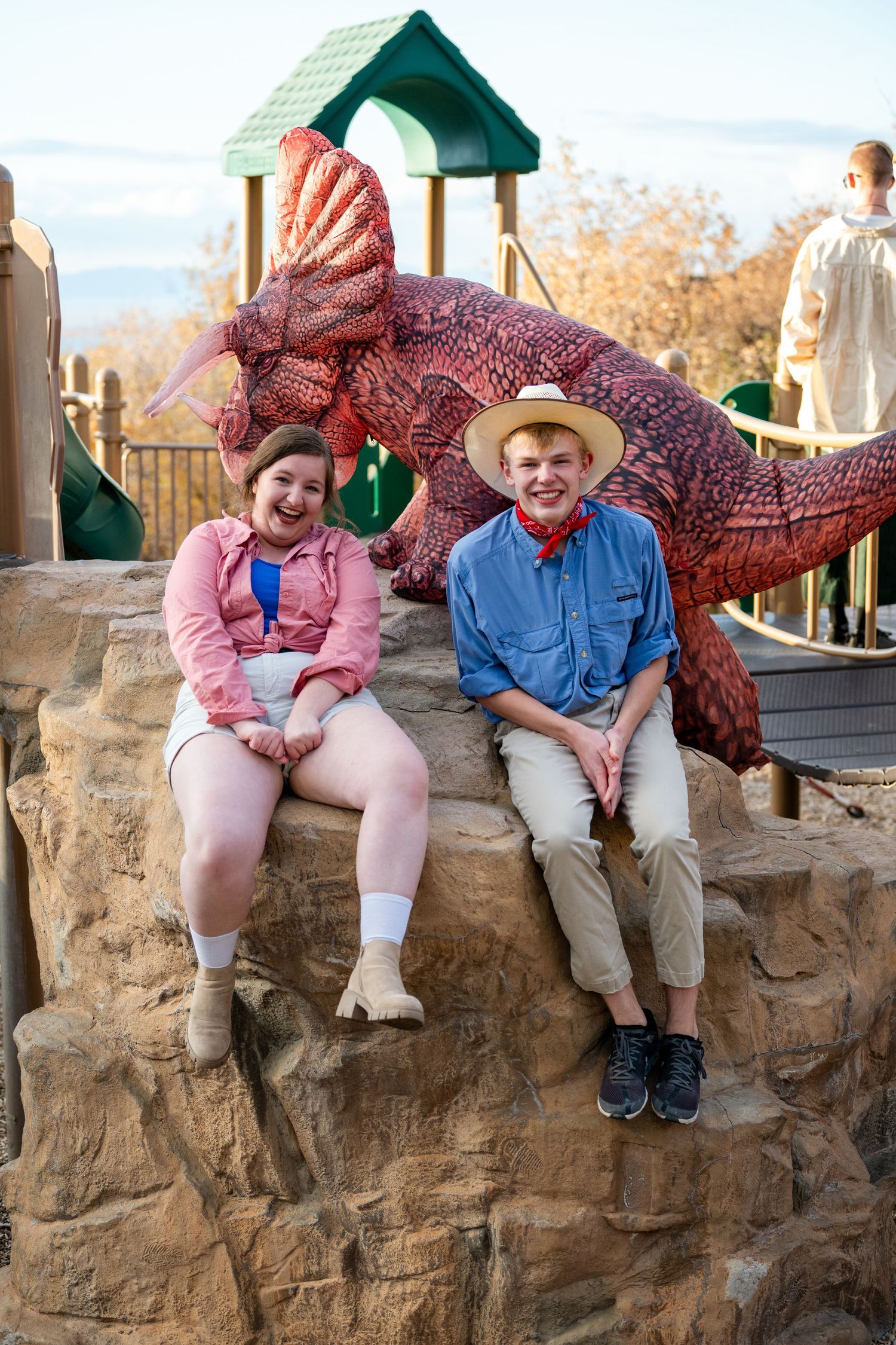 Two teens sitting on playground structure in Jurassic Park themed outfits with casual pose for Woods Cross dance