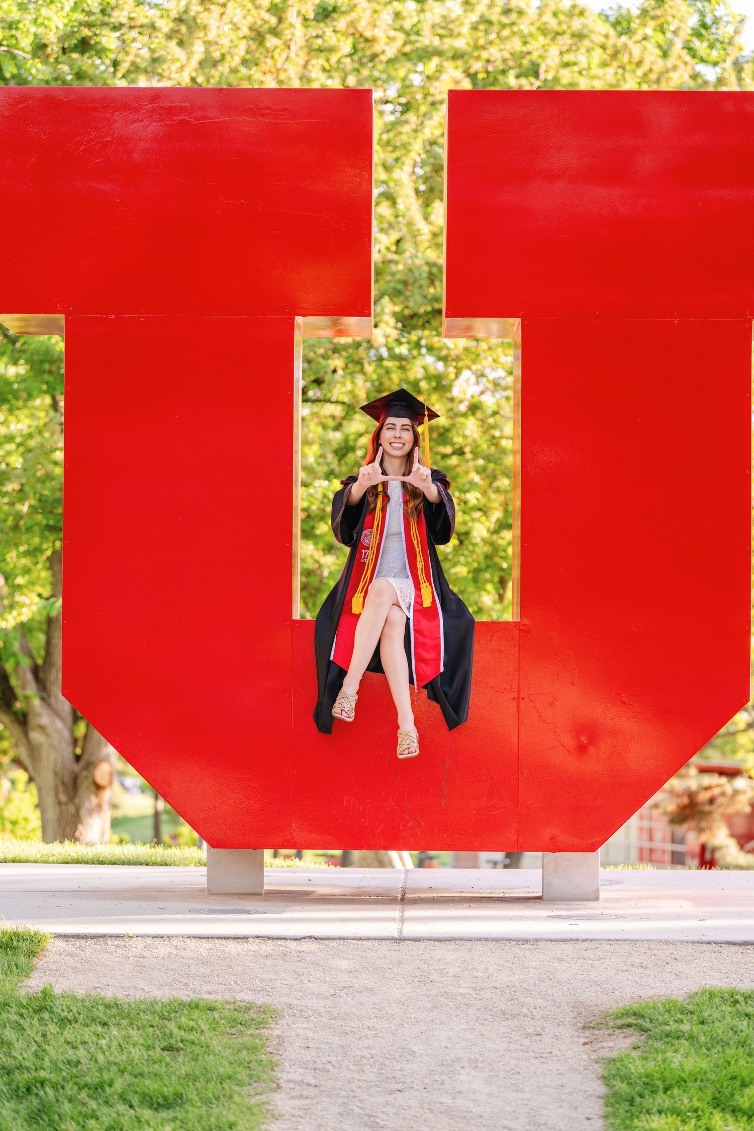 Graduate posing inside large red U sculpture in cap and gown on University of Utah campus
