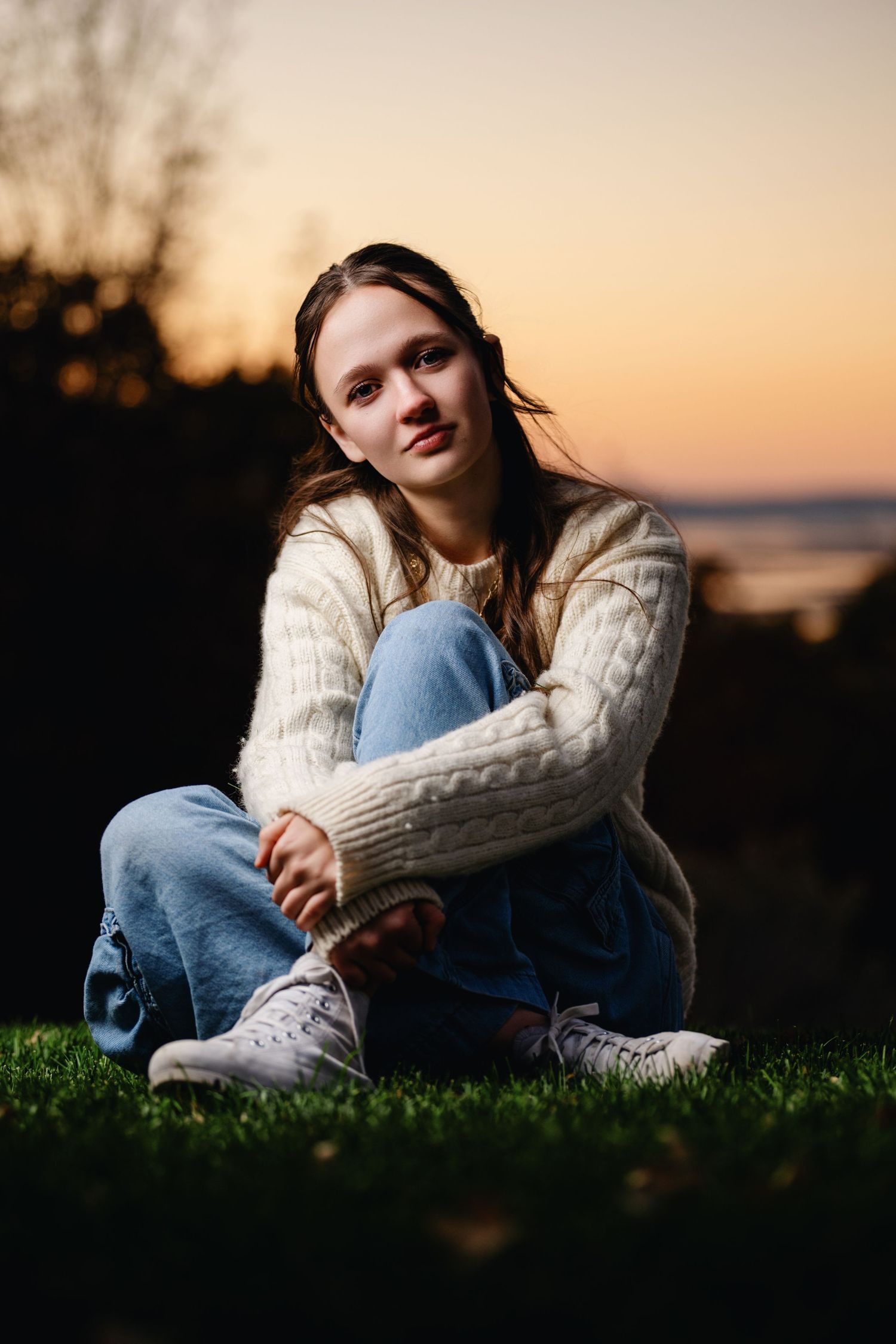 Teen girl sitting on grass at sunset with soft light and relaxed casual pose