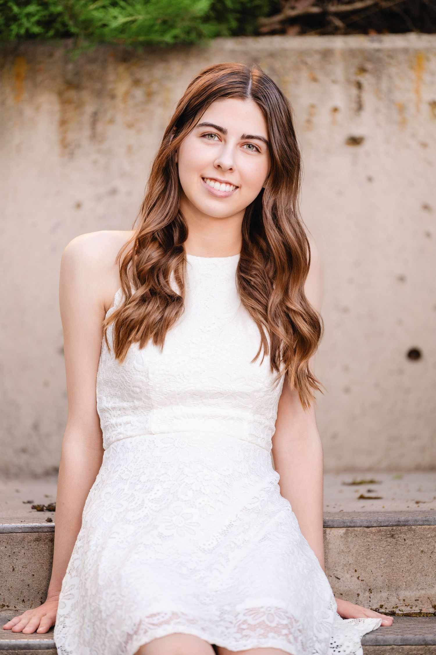 College girl in white dress sitting against textured wall with soft natural light