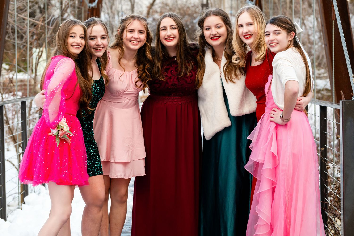 Group of girls in colorful dresses posing together on bridge in winter setting before the Sweethearts Dance at Woods Cross