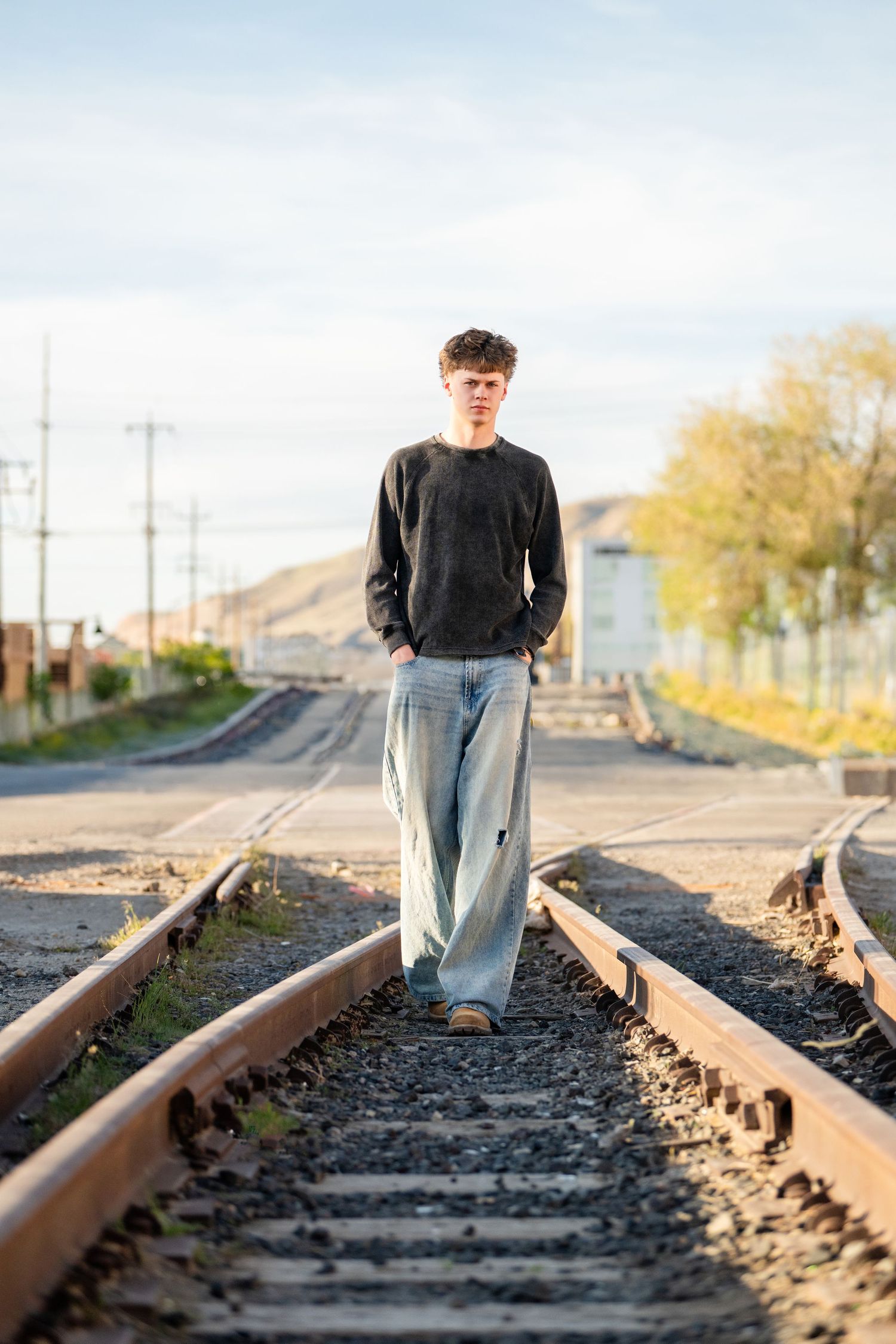 Senior boy walking on railroad tracks during urban Utah senior photography session