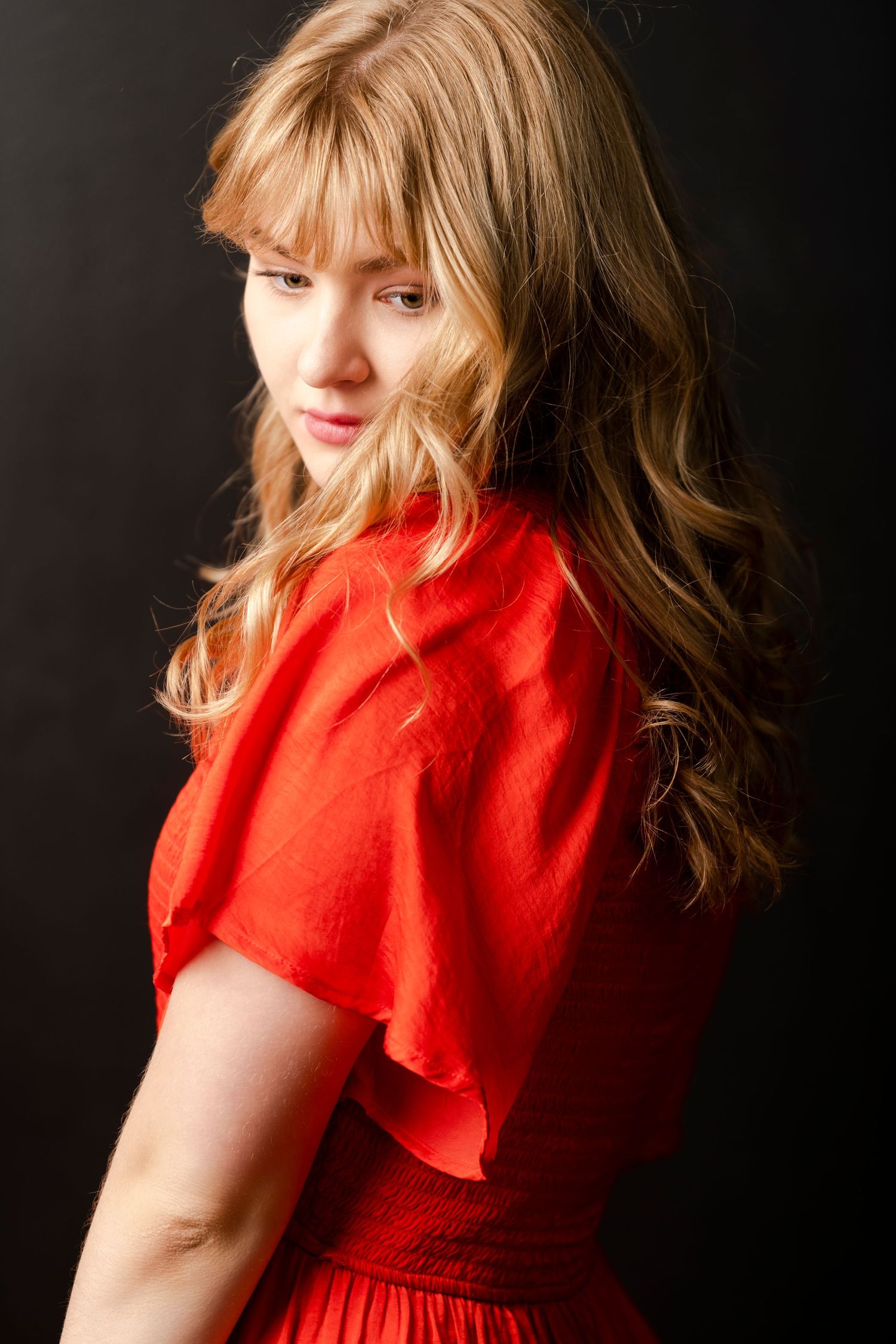 Studio portrait of young woman in red dress looking over shoulder with soft light and elegant mood