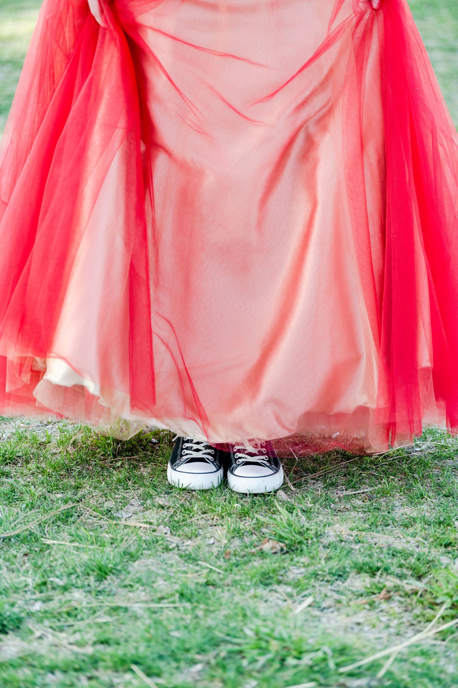 Close-up of red prom dress flowing over sneakers standing on grass for Woods Cross High School prom