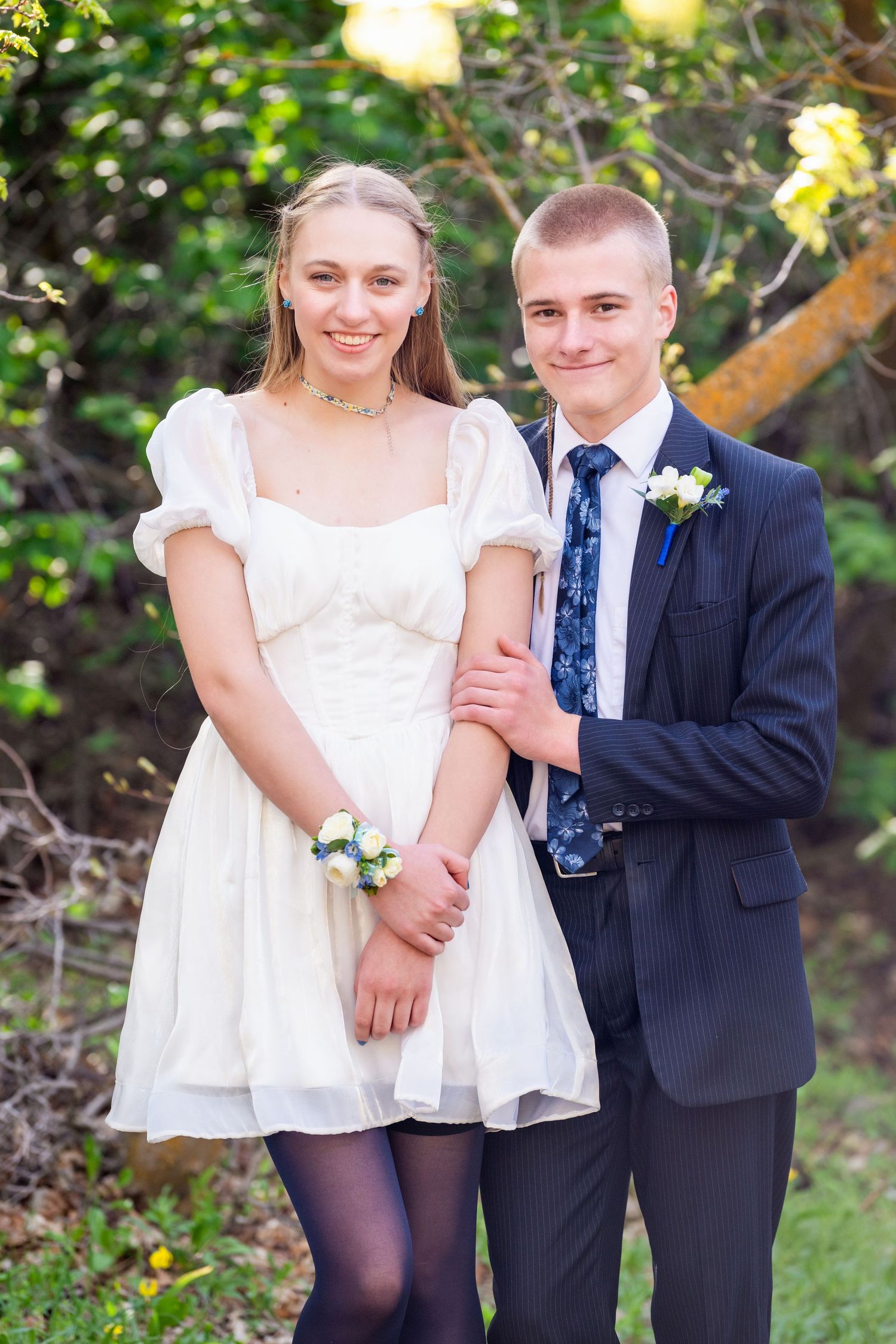 Prom couple smiling together in light dress and suit with natural greenery