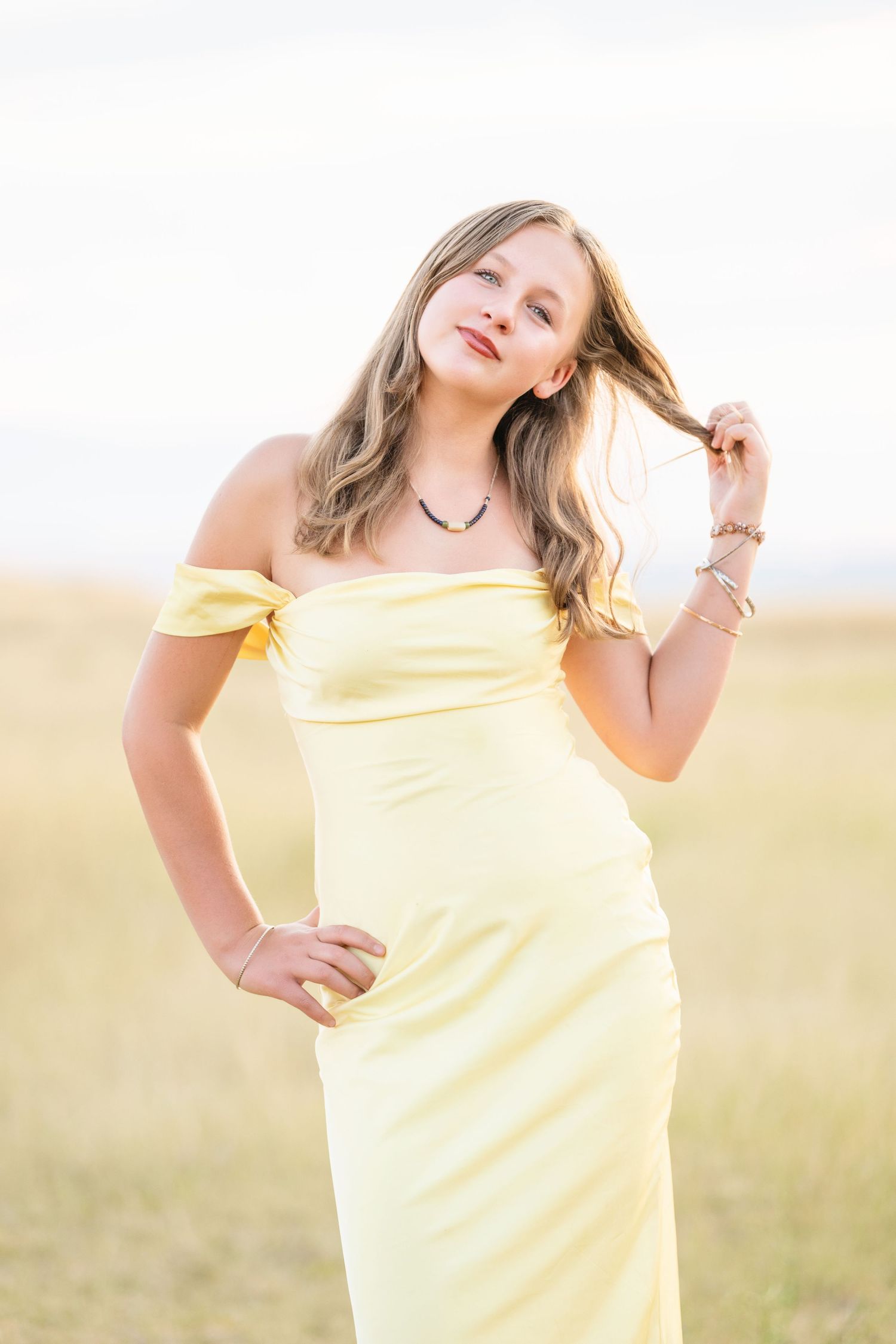 High school girl in yellow dress posing in open field with soft golden hour lighting