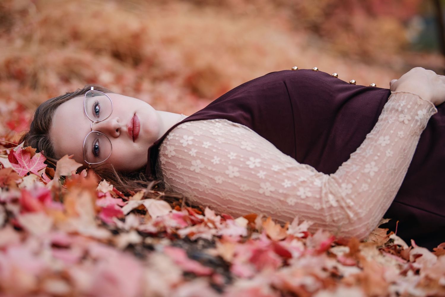 Senior girl lying in autumn leaves wearing maroon vest with soft natural light