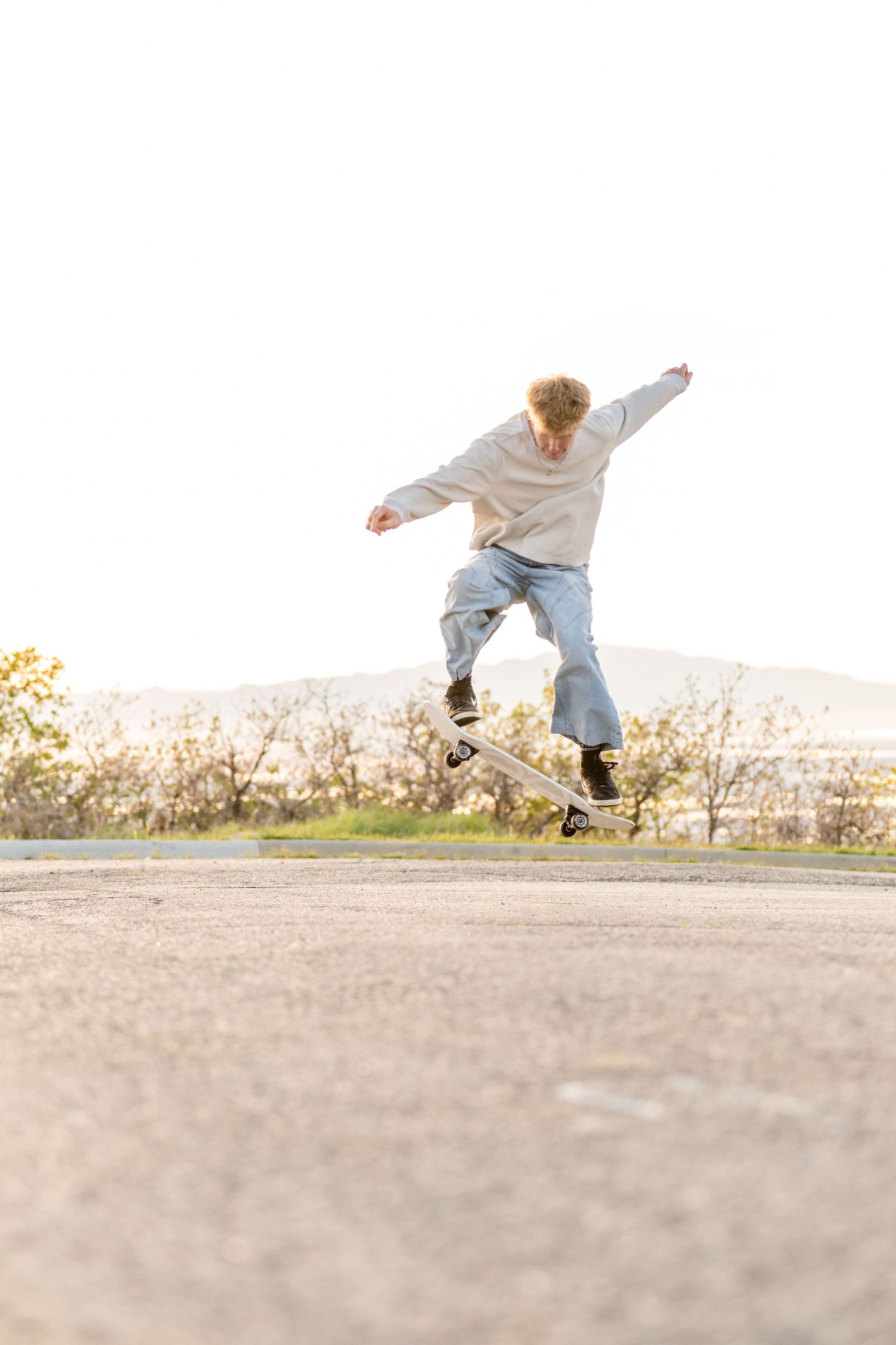 Creative action senior portrait of teenage boy doing skateboard tricks on road during Utah senior session