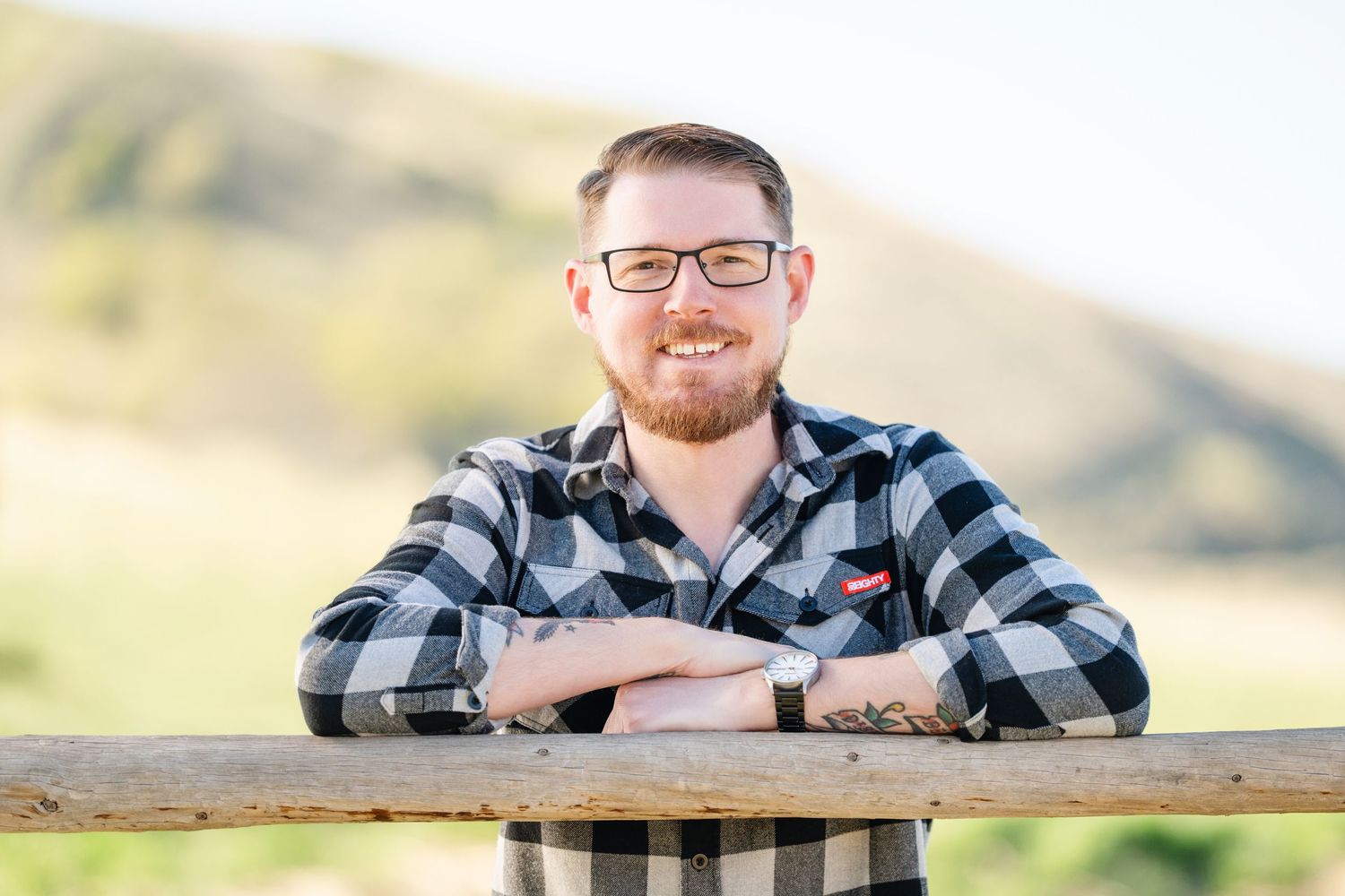 Outdoor portrait of man leaning on wooden fence with mountain scenery in the background