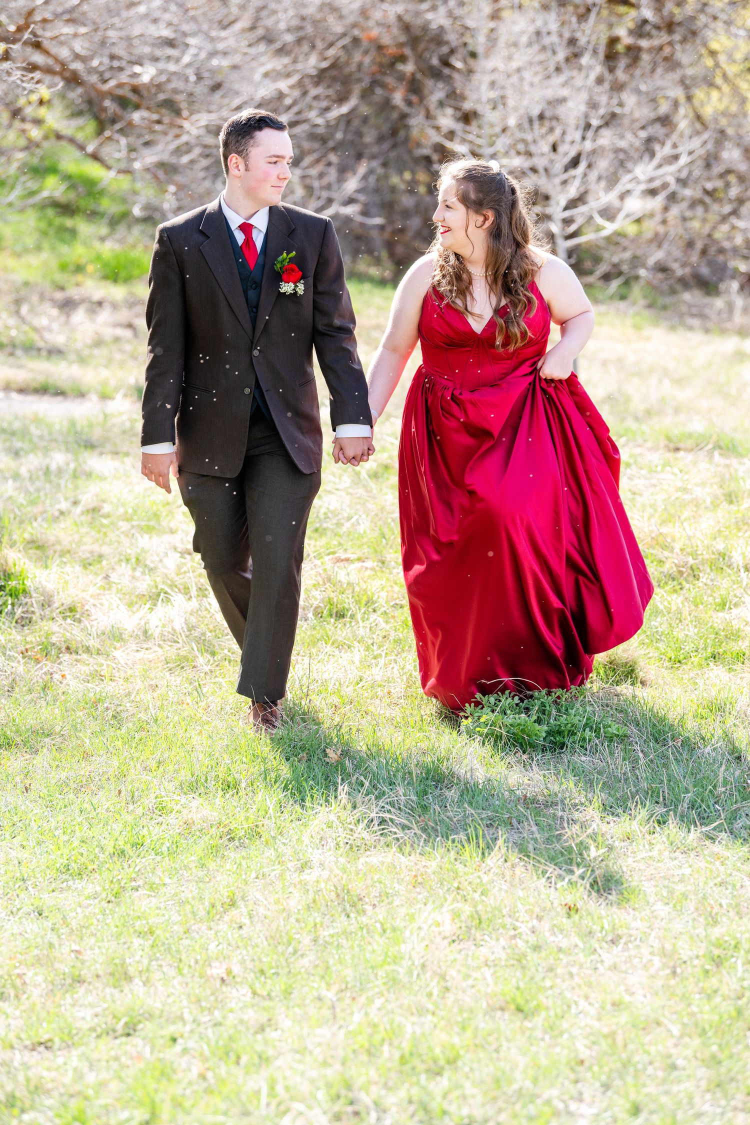 Prom couple walking together outdoors with flowing red dress and formal suit
