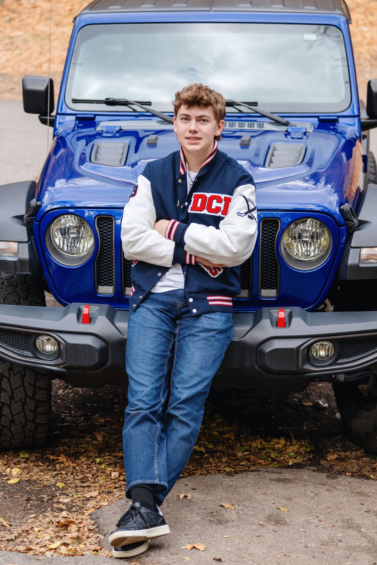 Senior boy leaning against blue Jeep wearing casual outfit with confident pose outdoors