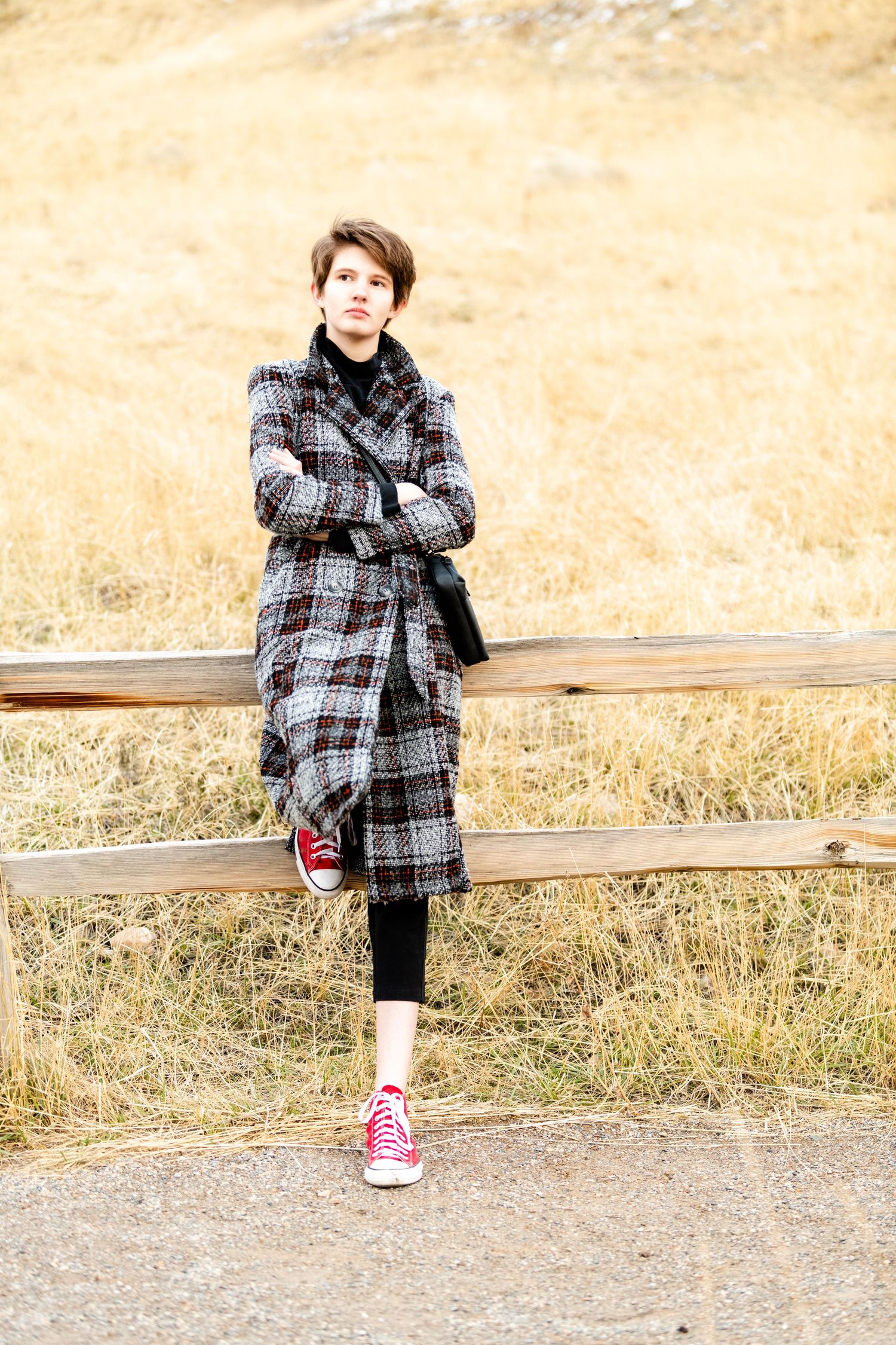 Senior girl standing by wooden fence wearing long coat with neutral outdoor tones