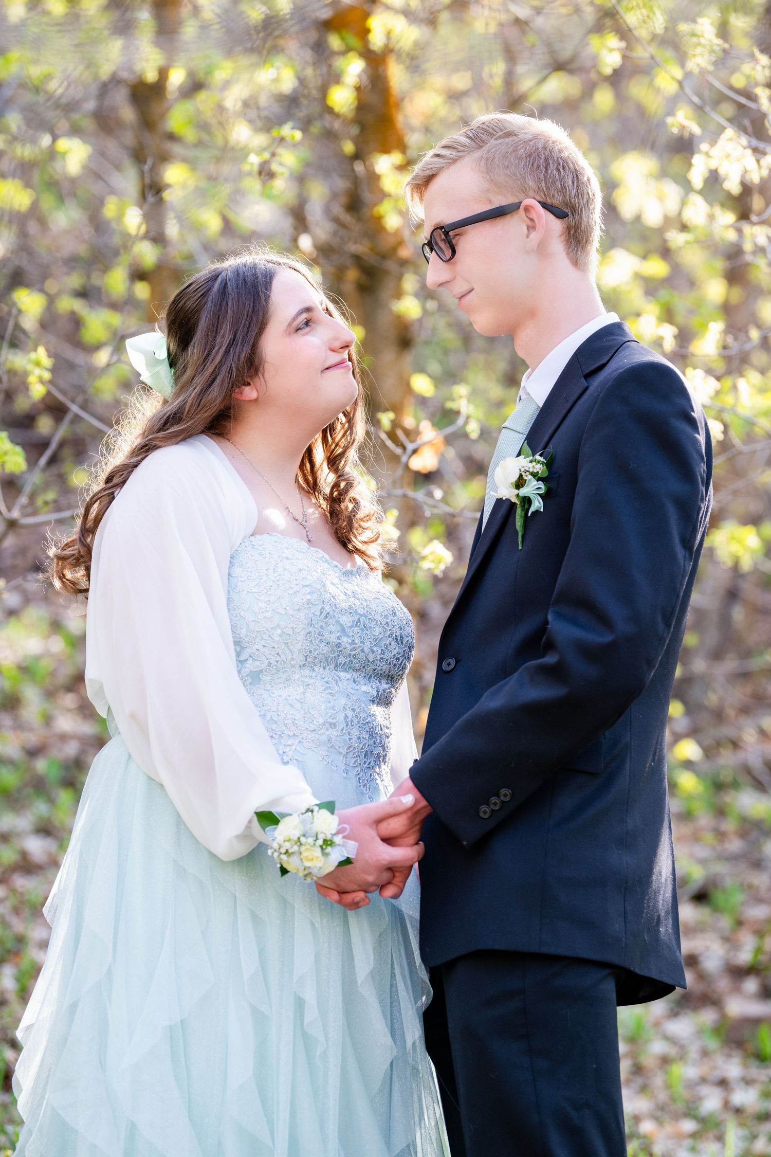 Prom couple facing each other holding hands in soft natural light outdoors