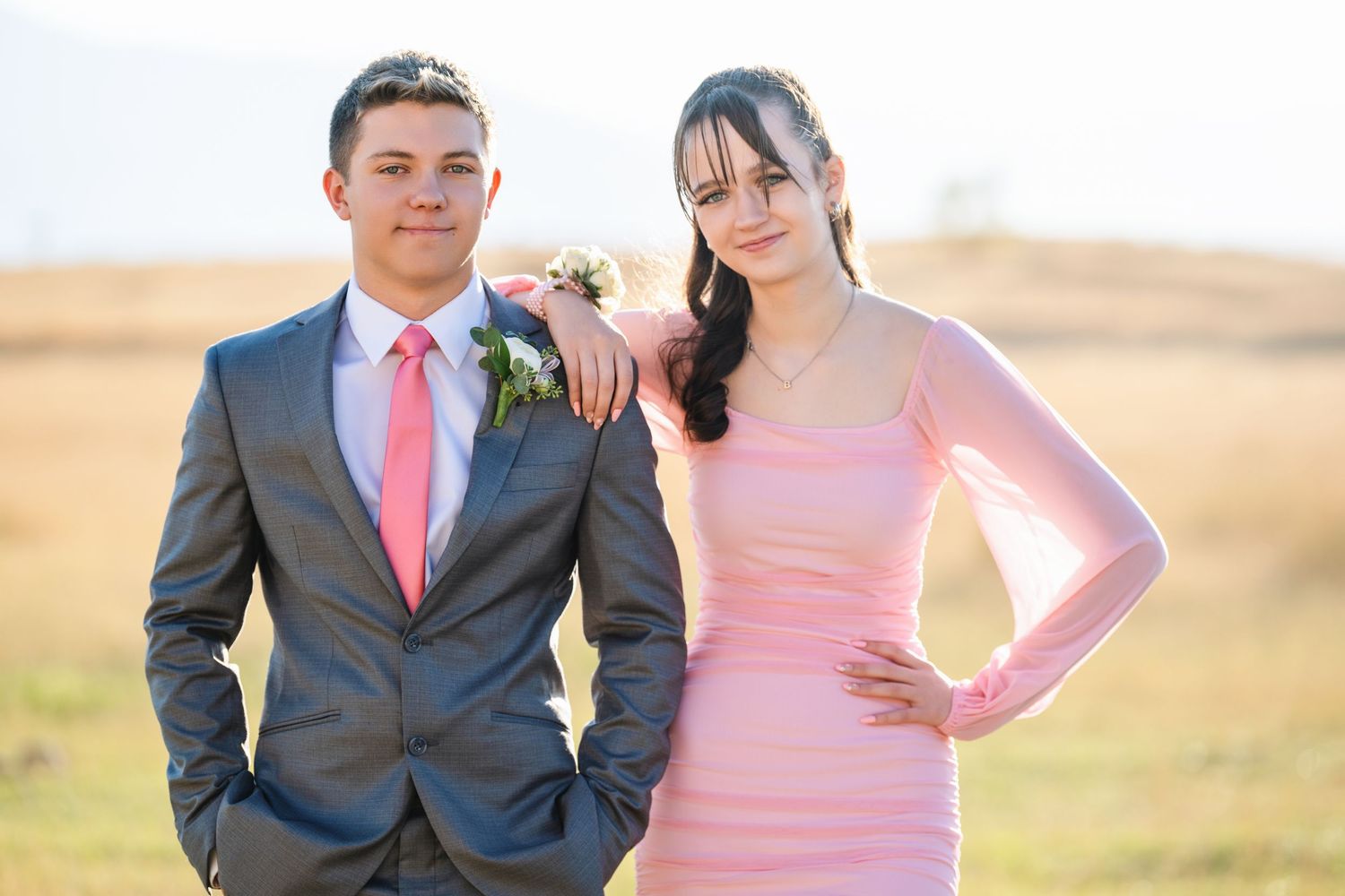 Homecoming couple posing in open field with pink dress and gray suit