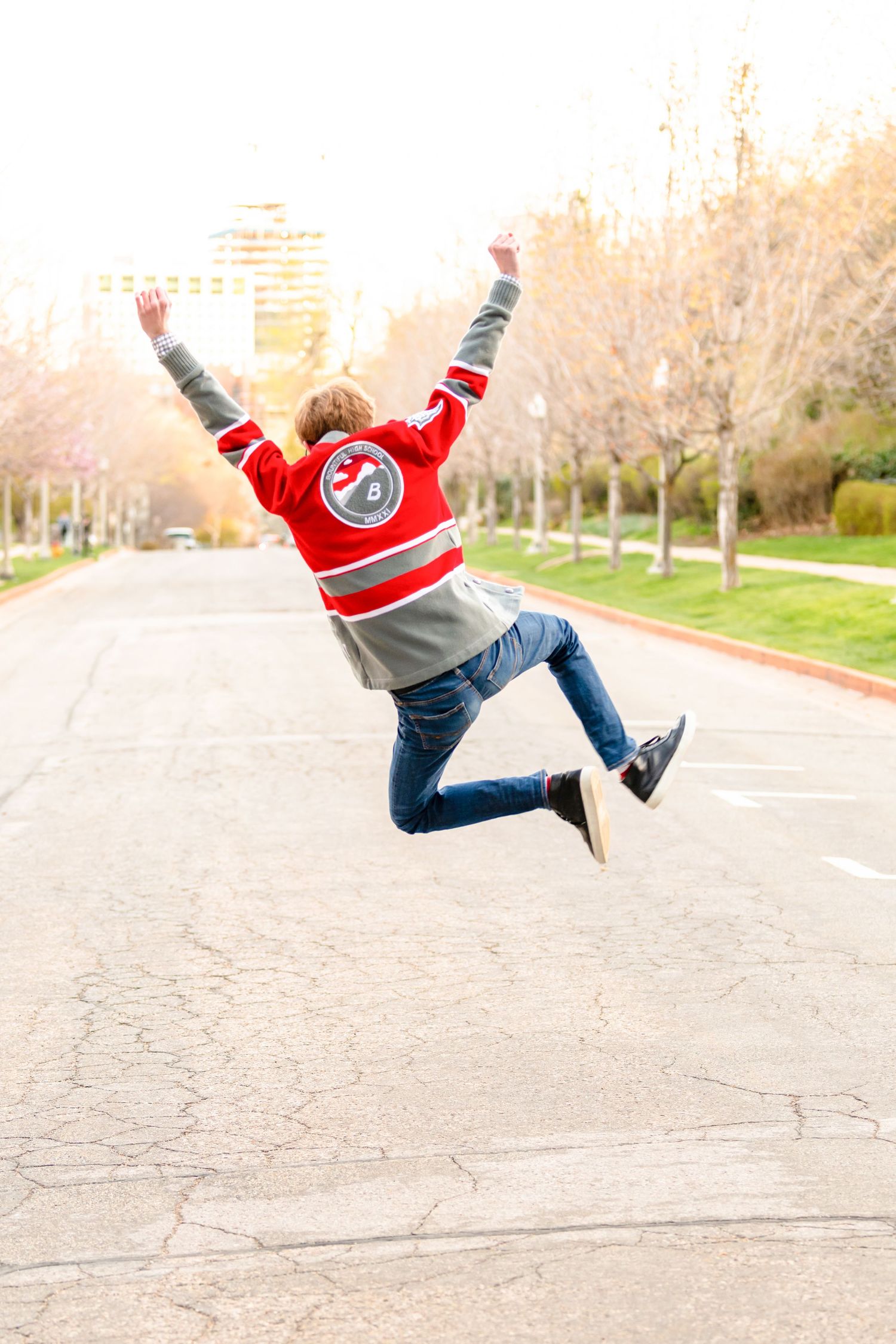 Senior boy jumping in Salt Lake City street wearing red sweater with playful energy and bright natural light